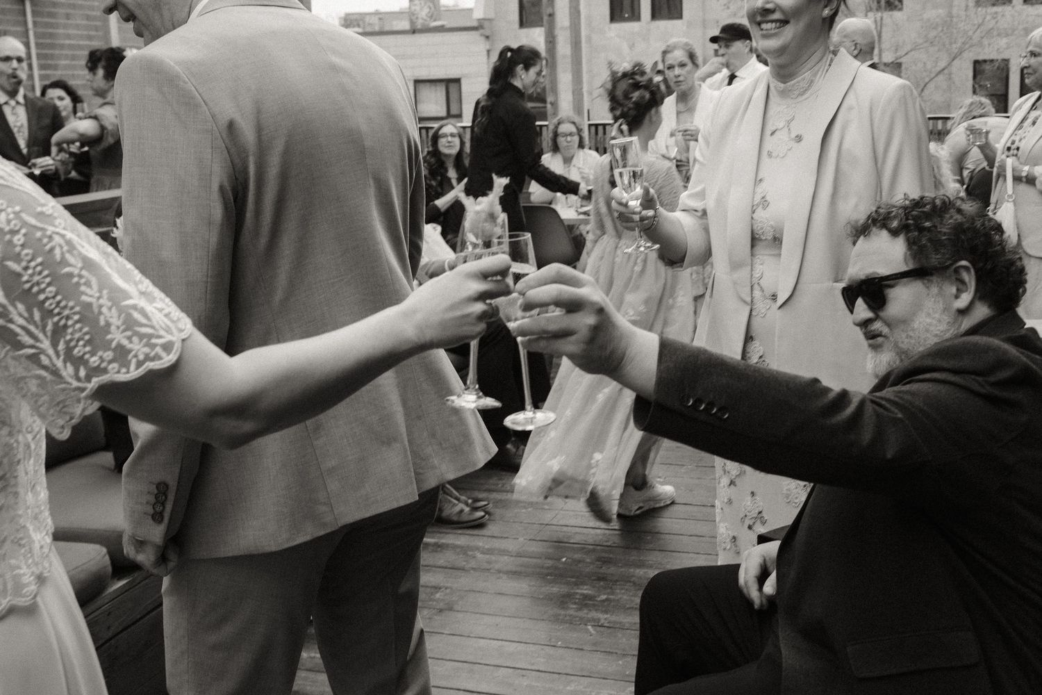 Wedding guests toast with champagne glasses at outdoor reception in black and white photo.