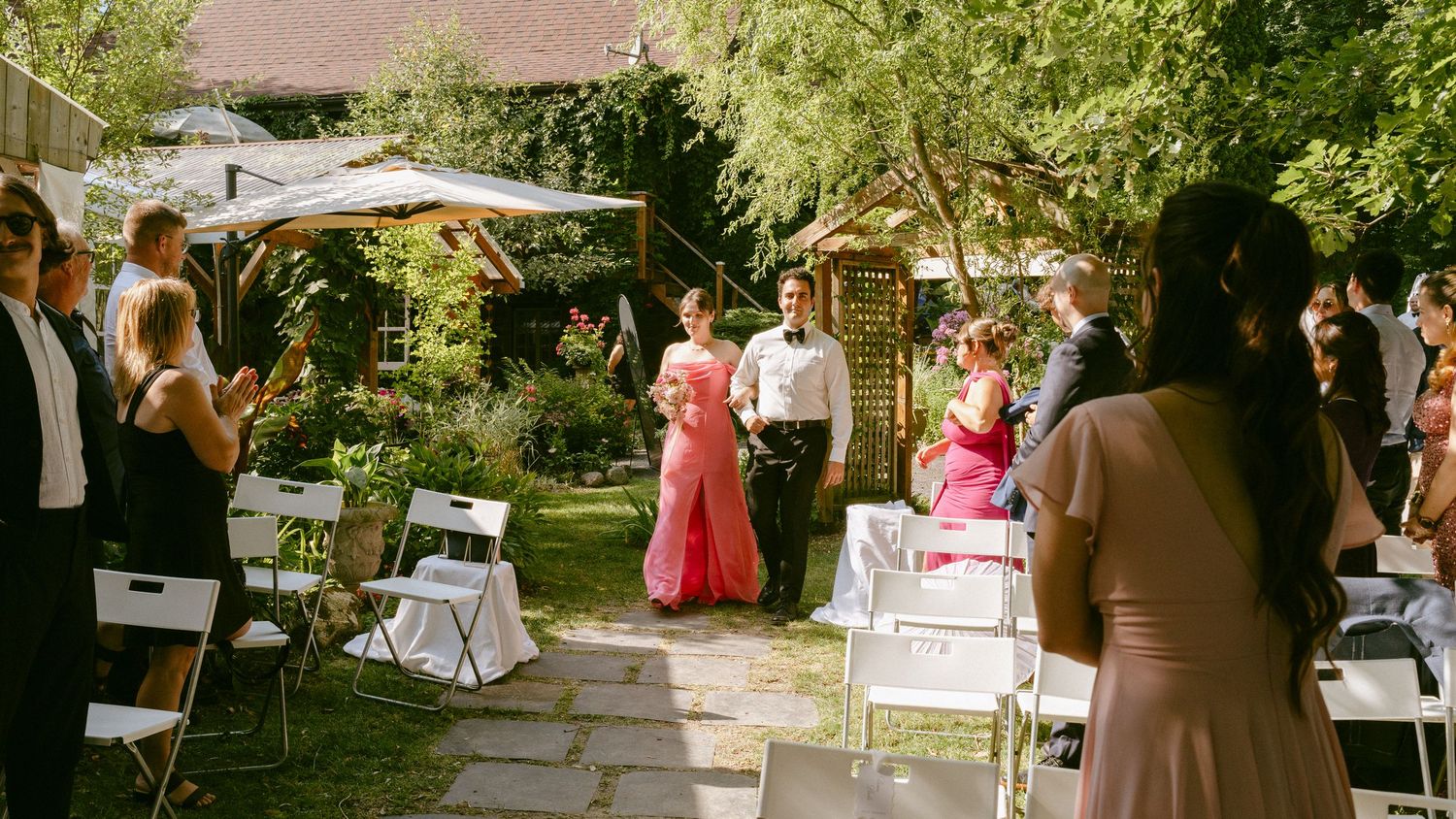 Guests applaud as wedding party walks down outdoor aisle during garden ceremony.