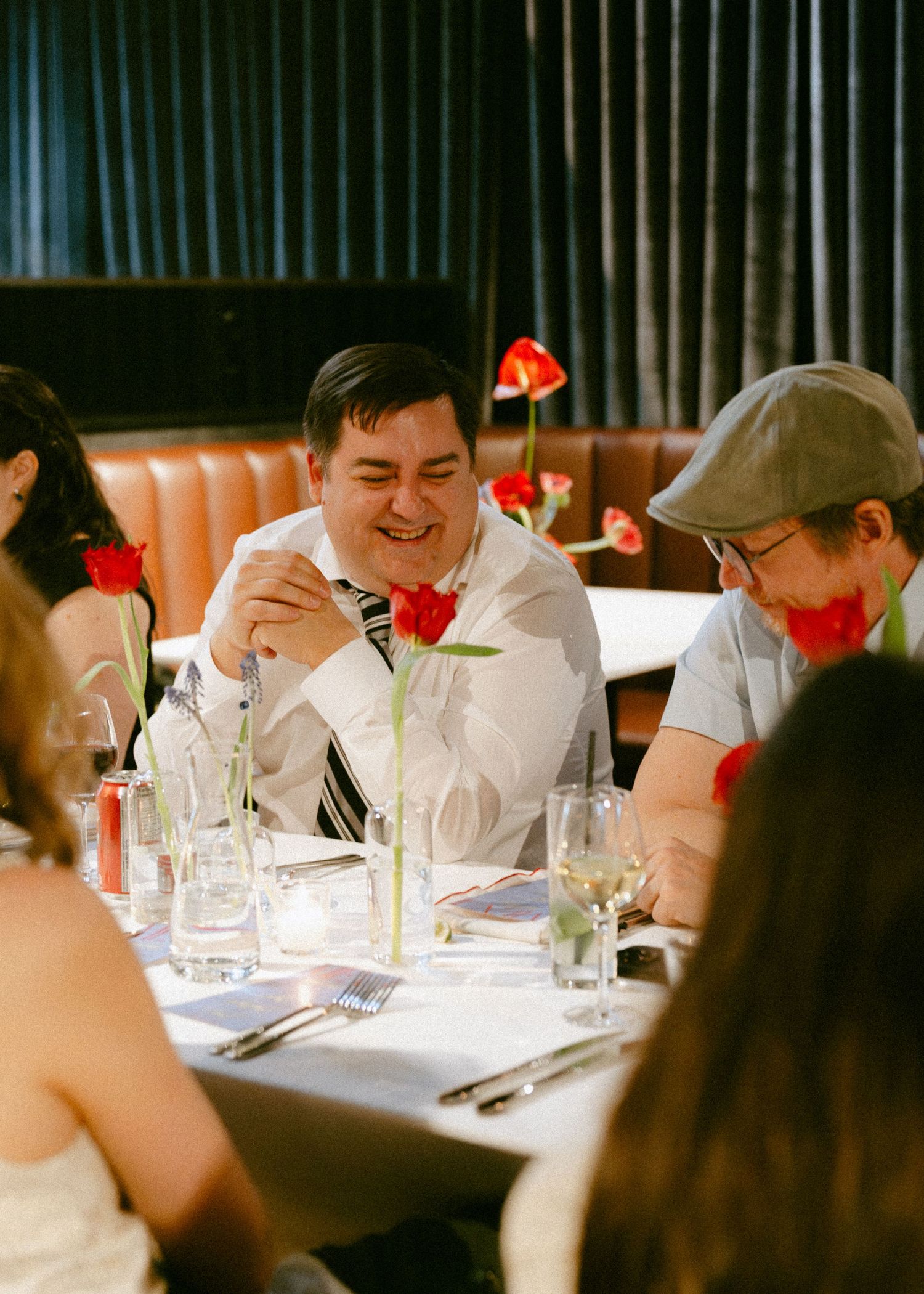 Man in white shirt laughing at wedding reception table with red tulip centerpieces.