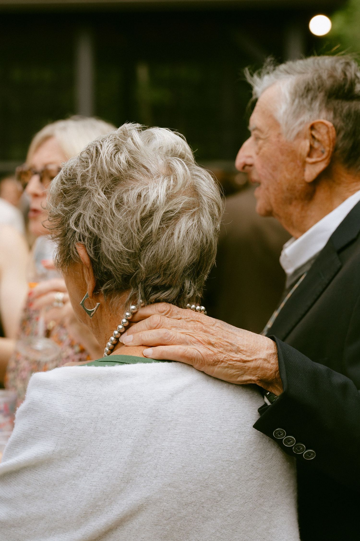Elderly couple sharing tender moment at wedding reception, man placing hand on womans shoulder.