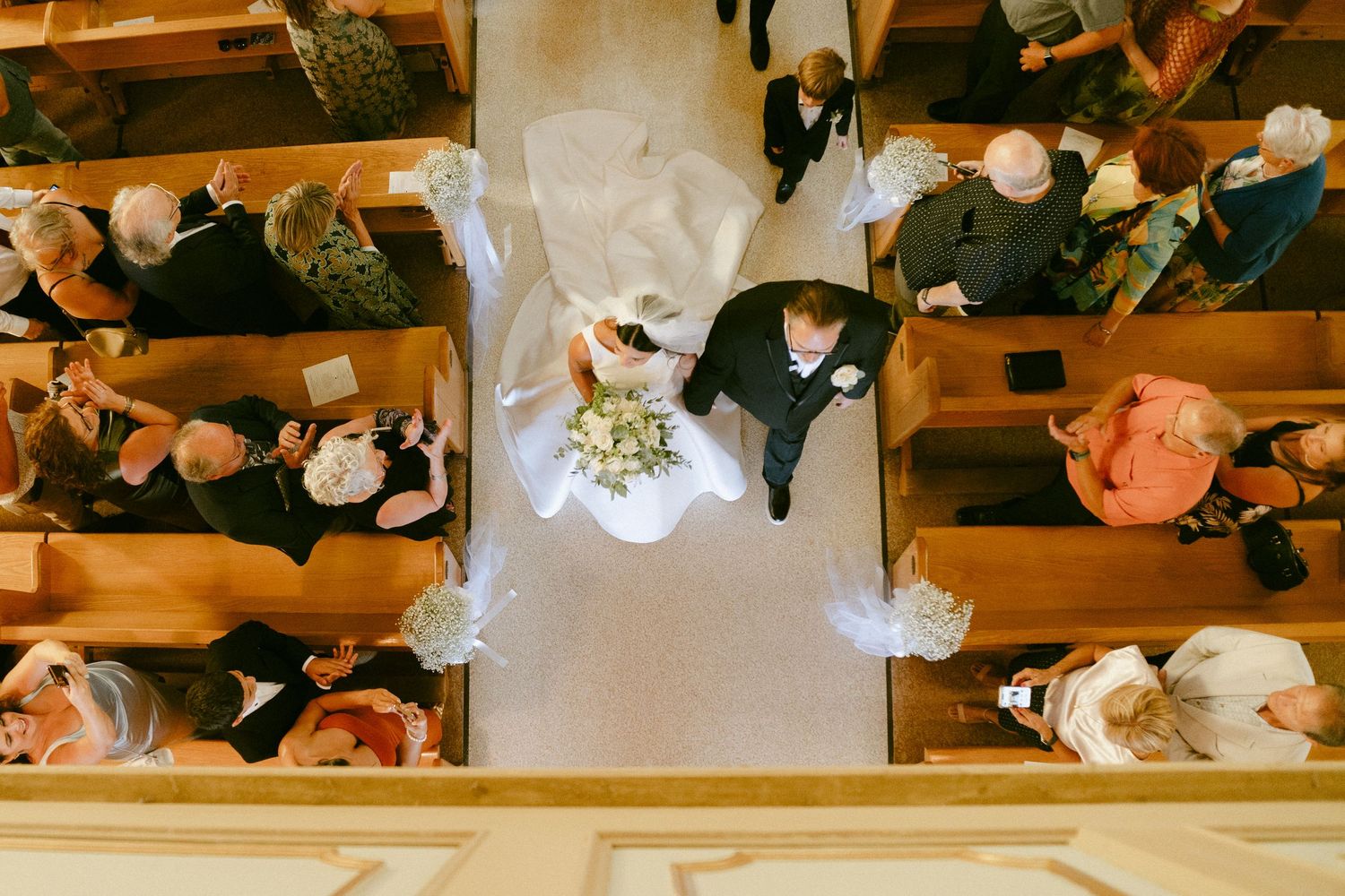 Aerial view of bride walking down church aisle with escort during traditional wedding ceremony.