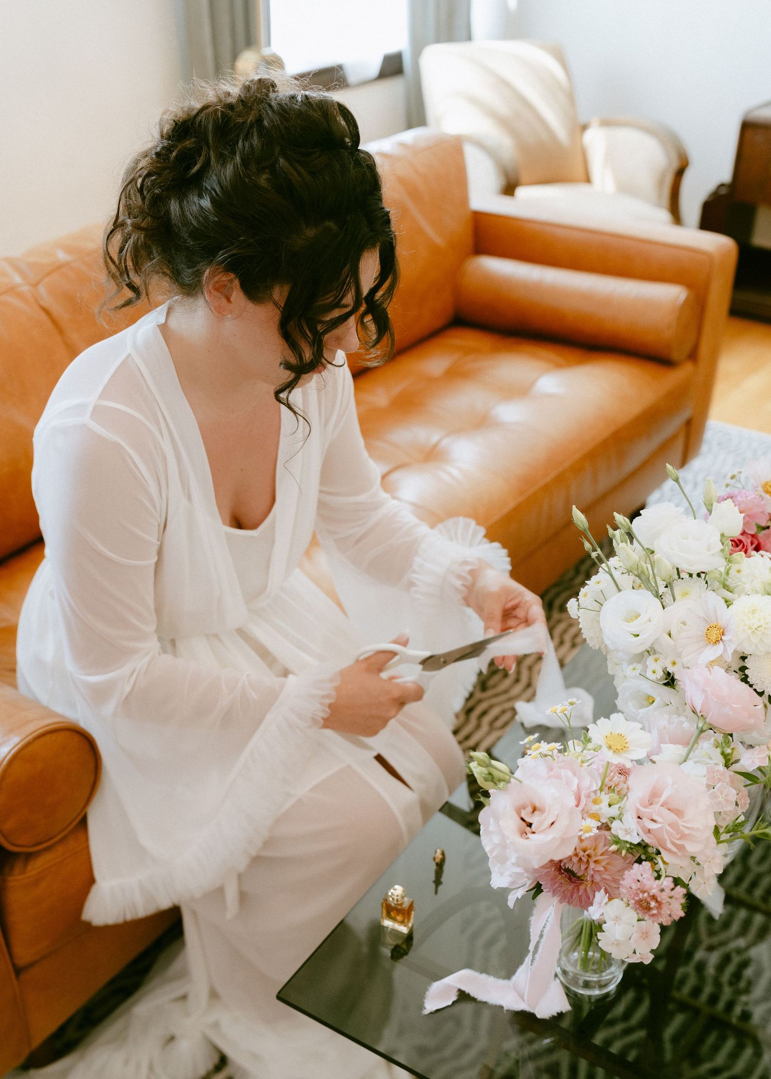 Bride in white robe reading a letter beside a bridal bouquet of pink and white flowers.