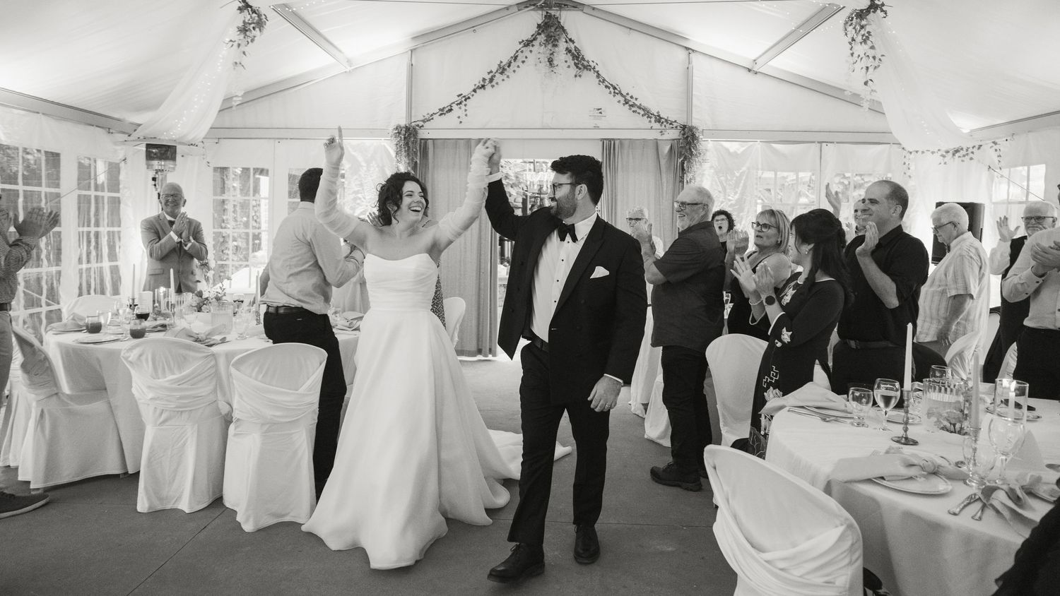 Bride and groom share first dance in elegant white tent wedding reception surrounded by celebrating guests.