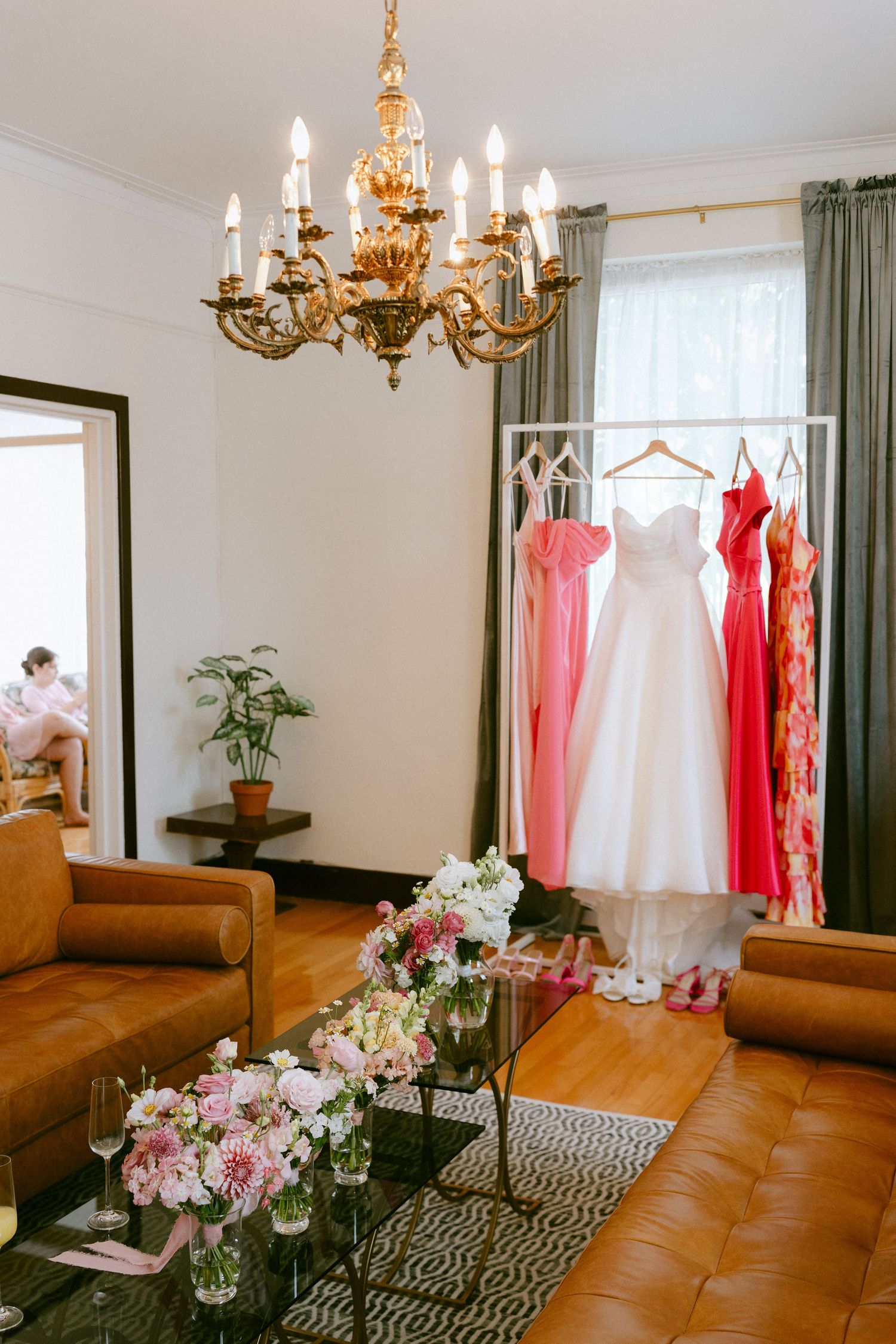 Wedding dresses and bridesmaid gowns on a rack in a elegant room with gold chandelier.
