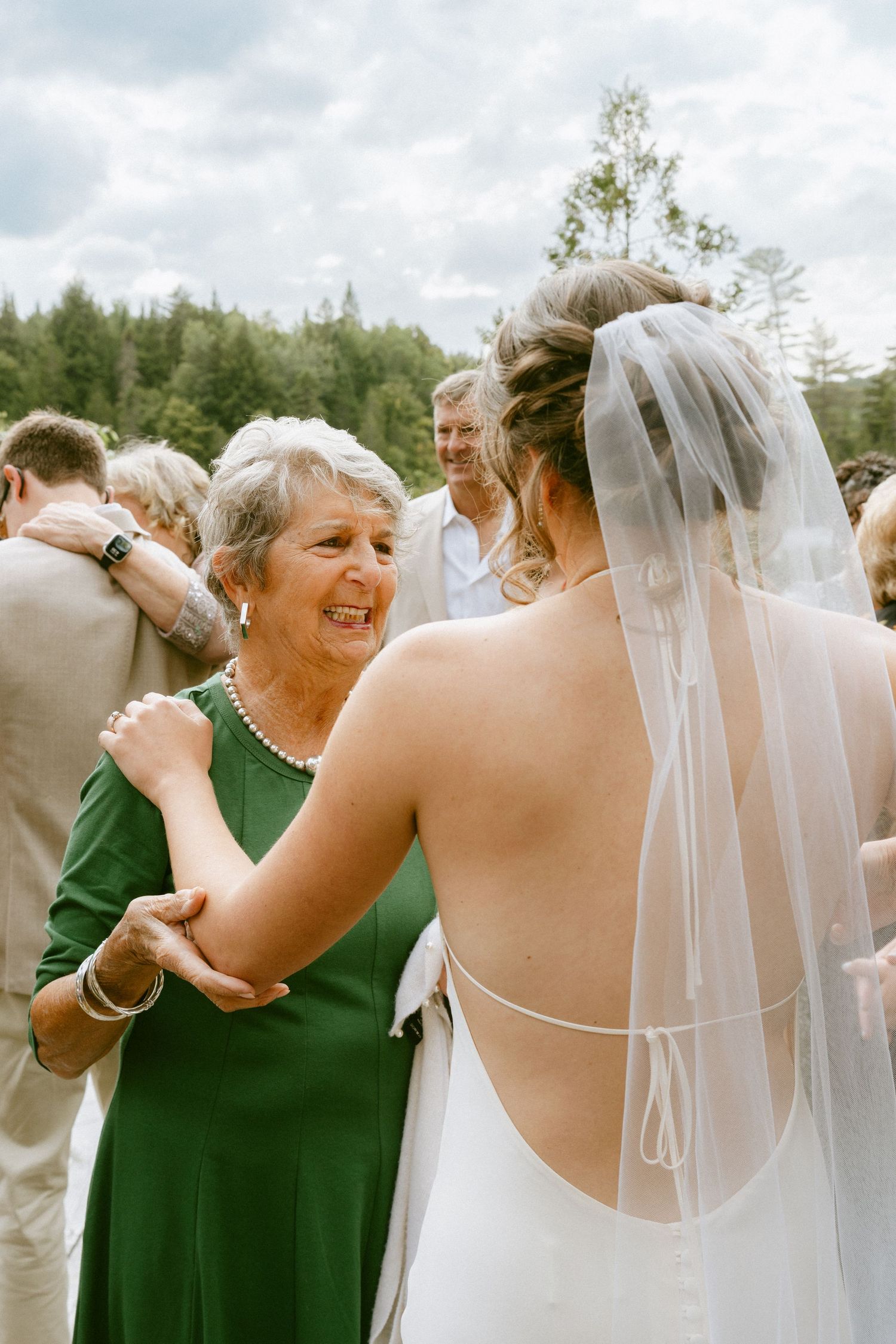 Elderly woman in green dress warmly embraces the bride after an outdoor wedding ceremony.