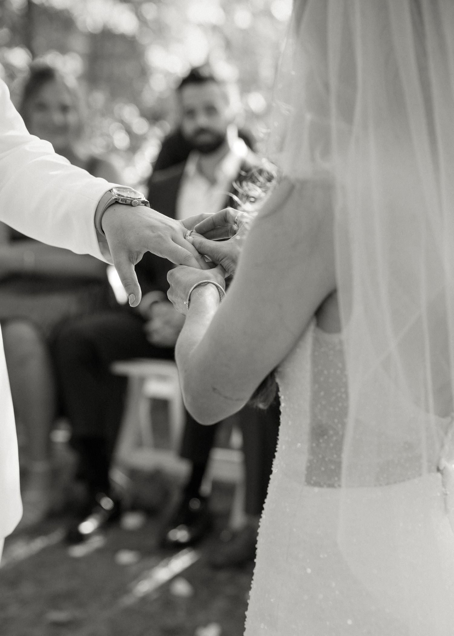 Black and white close-up of two brides holding hands during outdoor wedding ceremony.