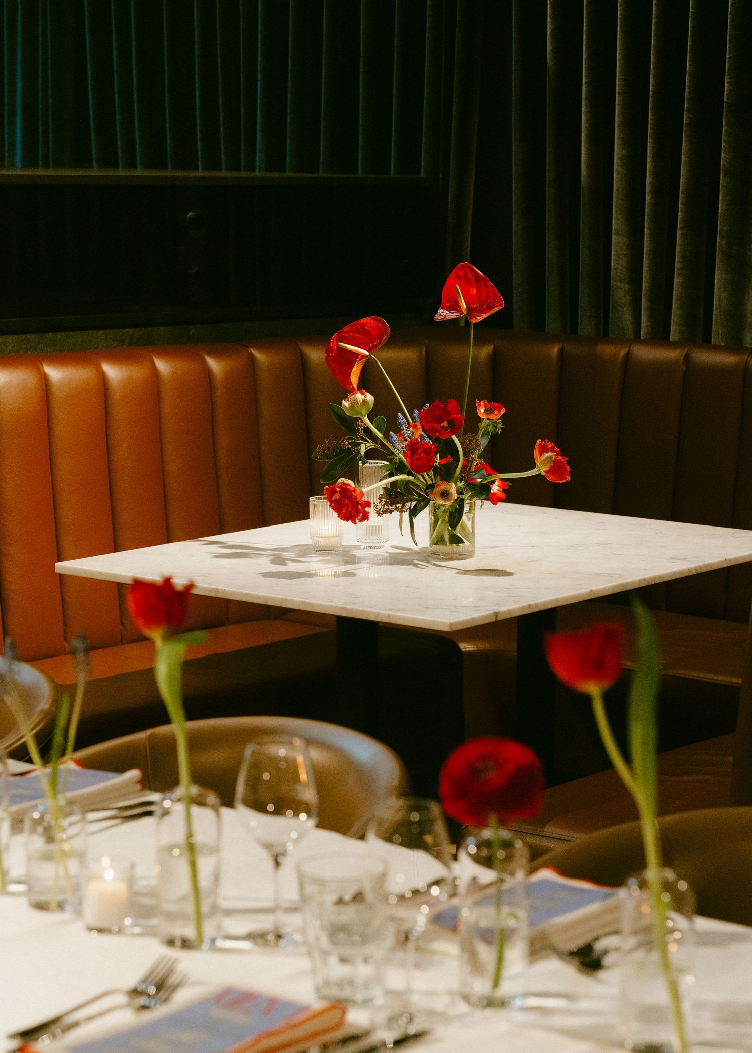 Elegant restaurant table set with red tulips and anthurium flowers in glass vases.