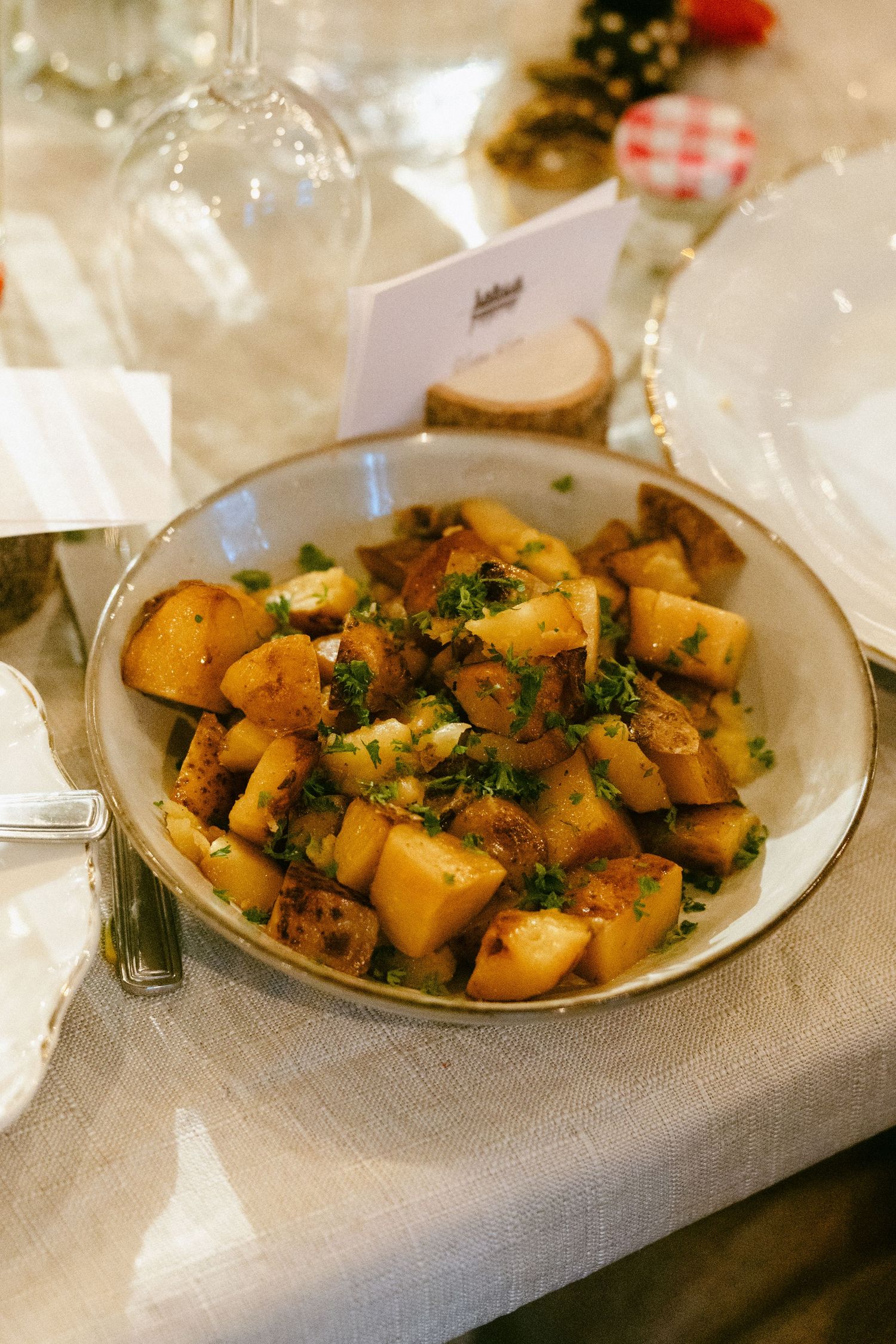 Bowl of roasted herb potatoes served on a linen-covered wedding reception dinner table.