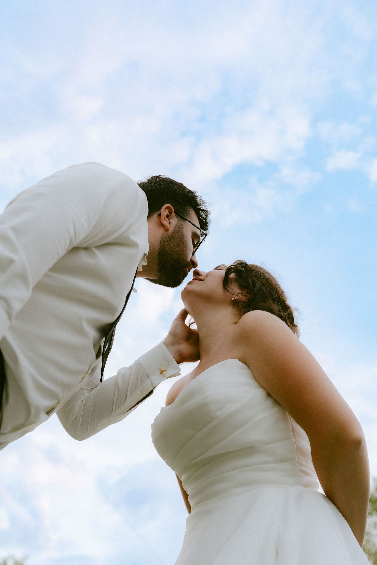 Bride and groom sharing a romantic kiss under a bright blue sky.