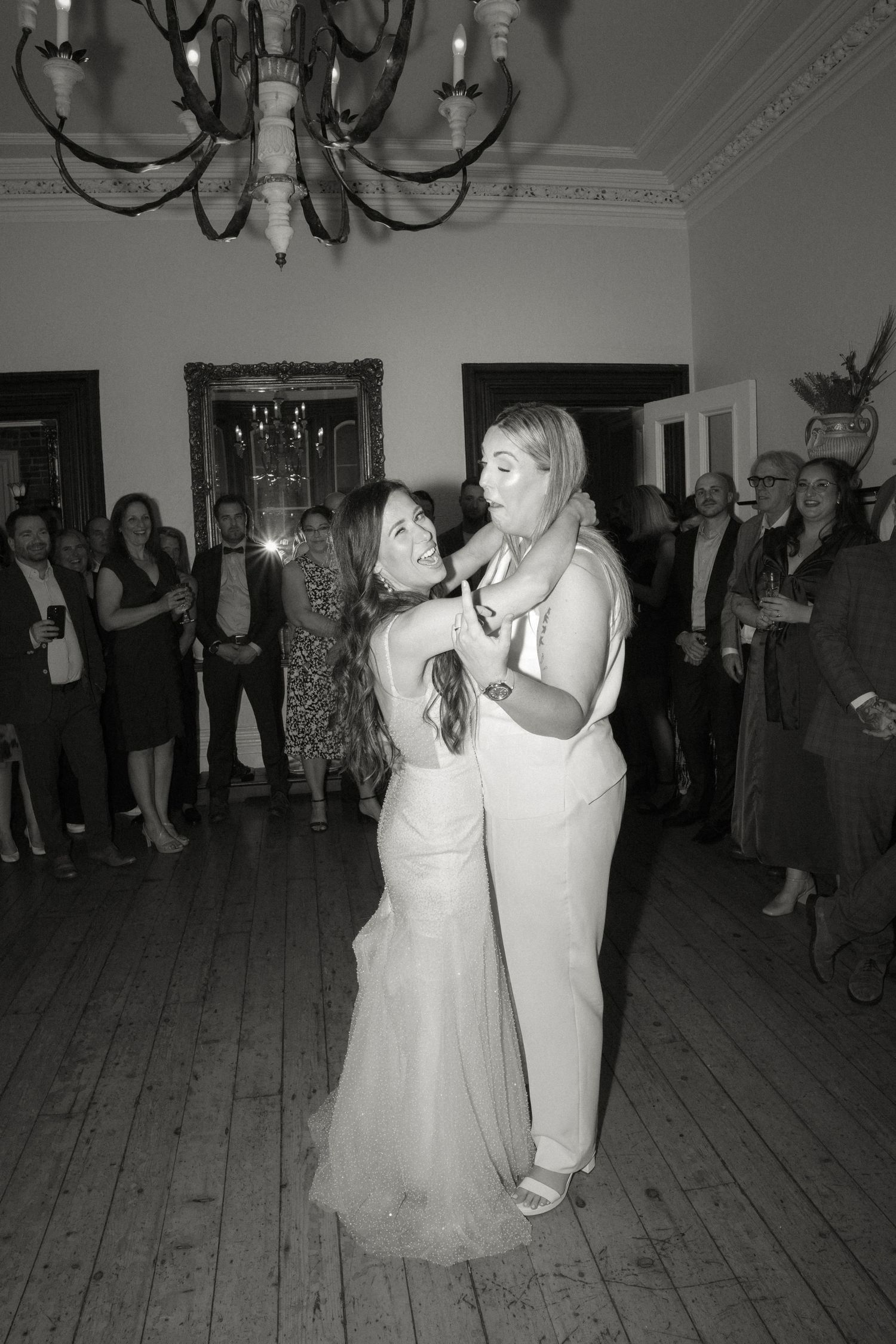 Black and white photo of two brides laughing during first dance at elegant wedding reception.