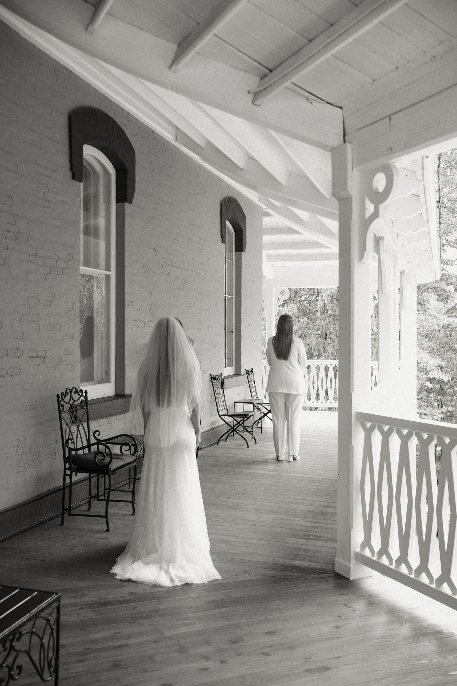 Bride in white gown and veil standing on Victorian venue porch.