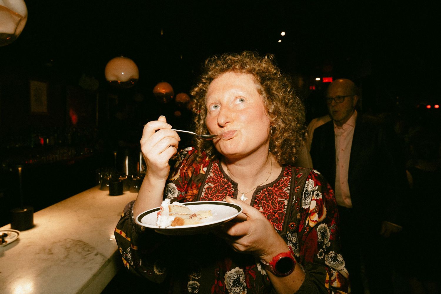 A woman with curly hair enjoys a bowl of soup at a dimly lit restaurant bar.