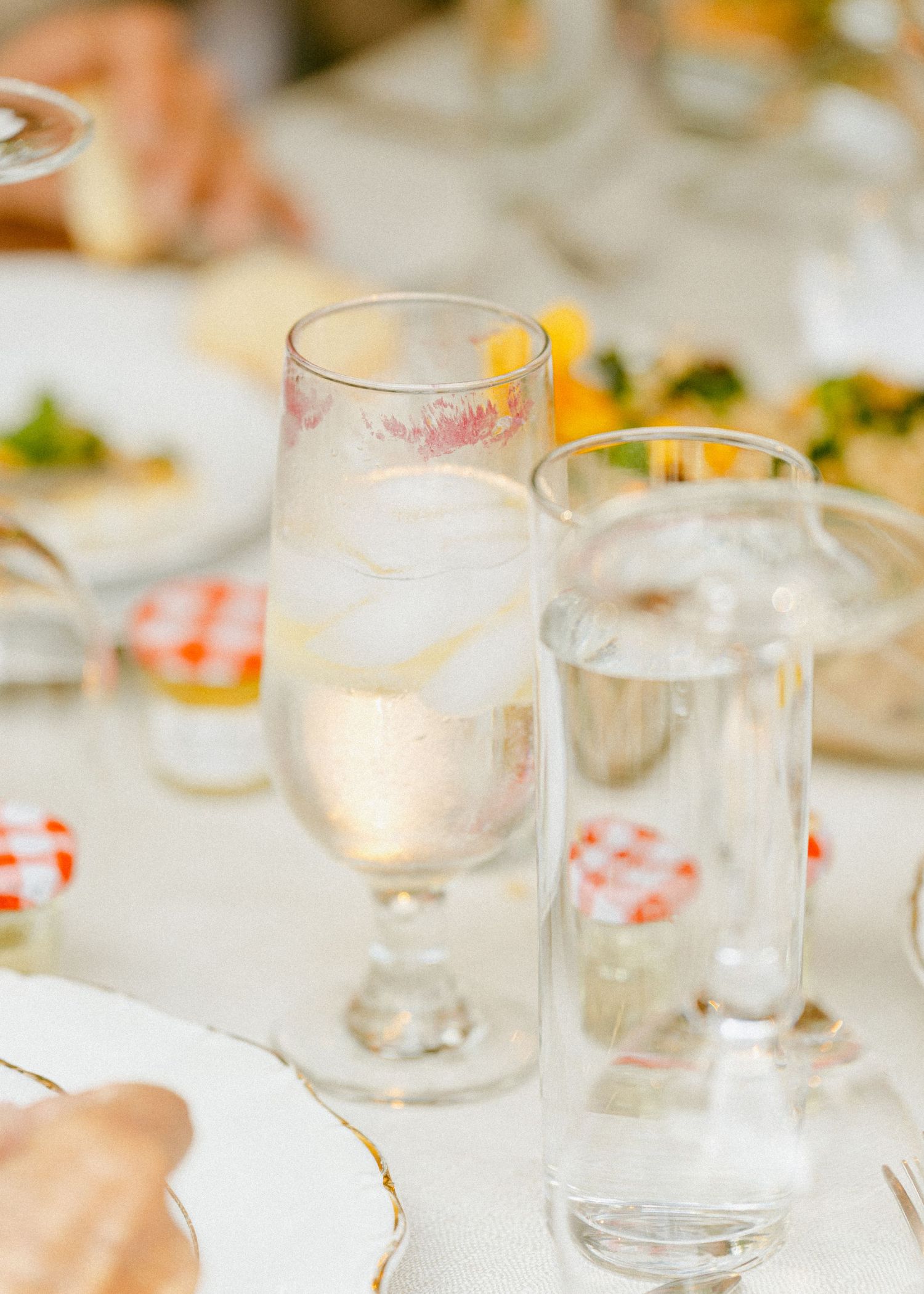 Elegant wedding reception table setting with crystal glassware, water glasses, and colorful food dishes in soft focus.