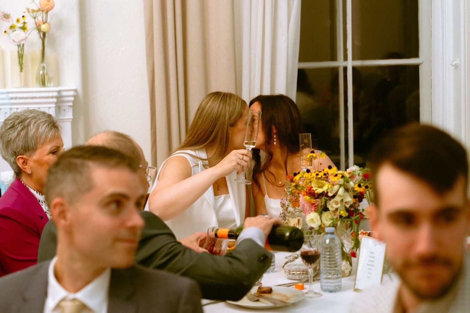 Two women sharing a quiet moment at a wedding reception dinner table.