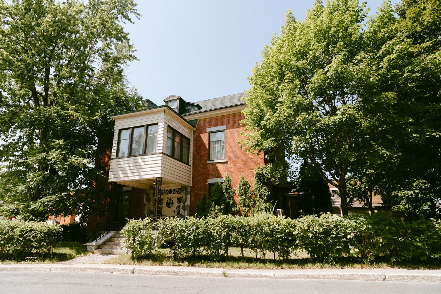 Elegant red brick wedding venue surrounded by lush green trees on a sunny day.