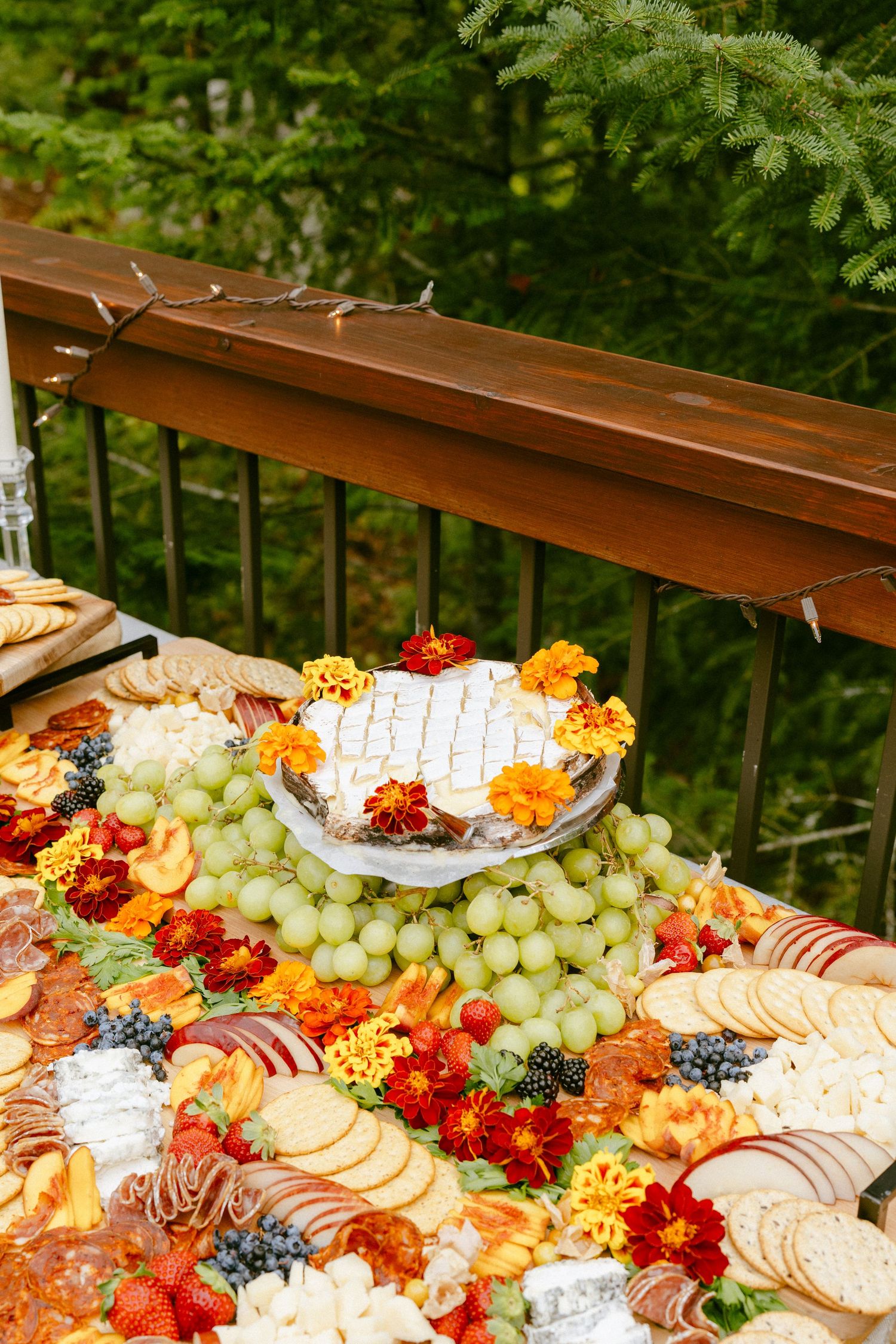 Elaborate outdoor wedding grazing table featuring cheeses, charcuterie, fruits, crackers, and fresh flowers.