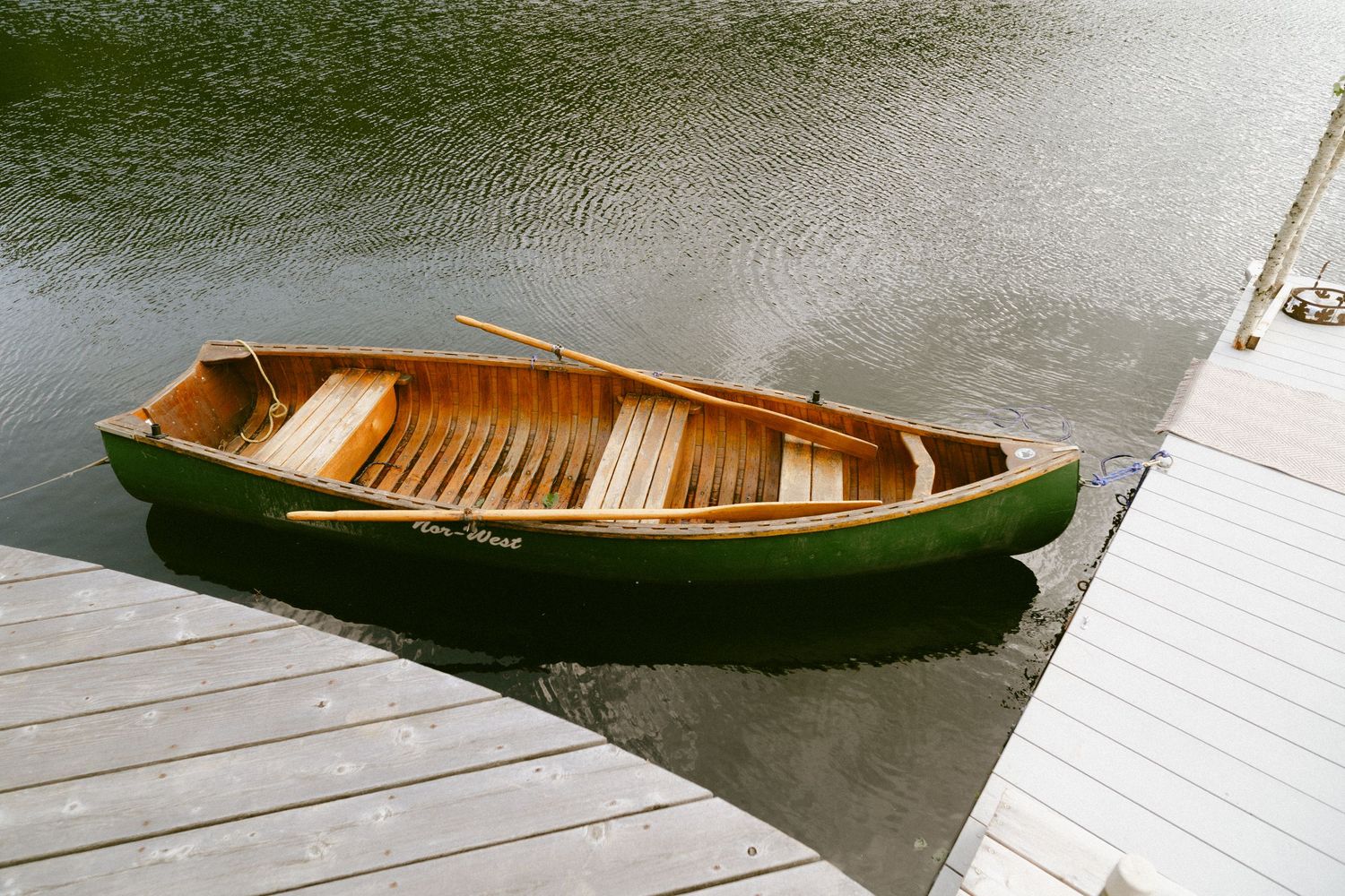 Classic green wooden rowboat with oars docked beside a wooden pier on calm water.