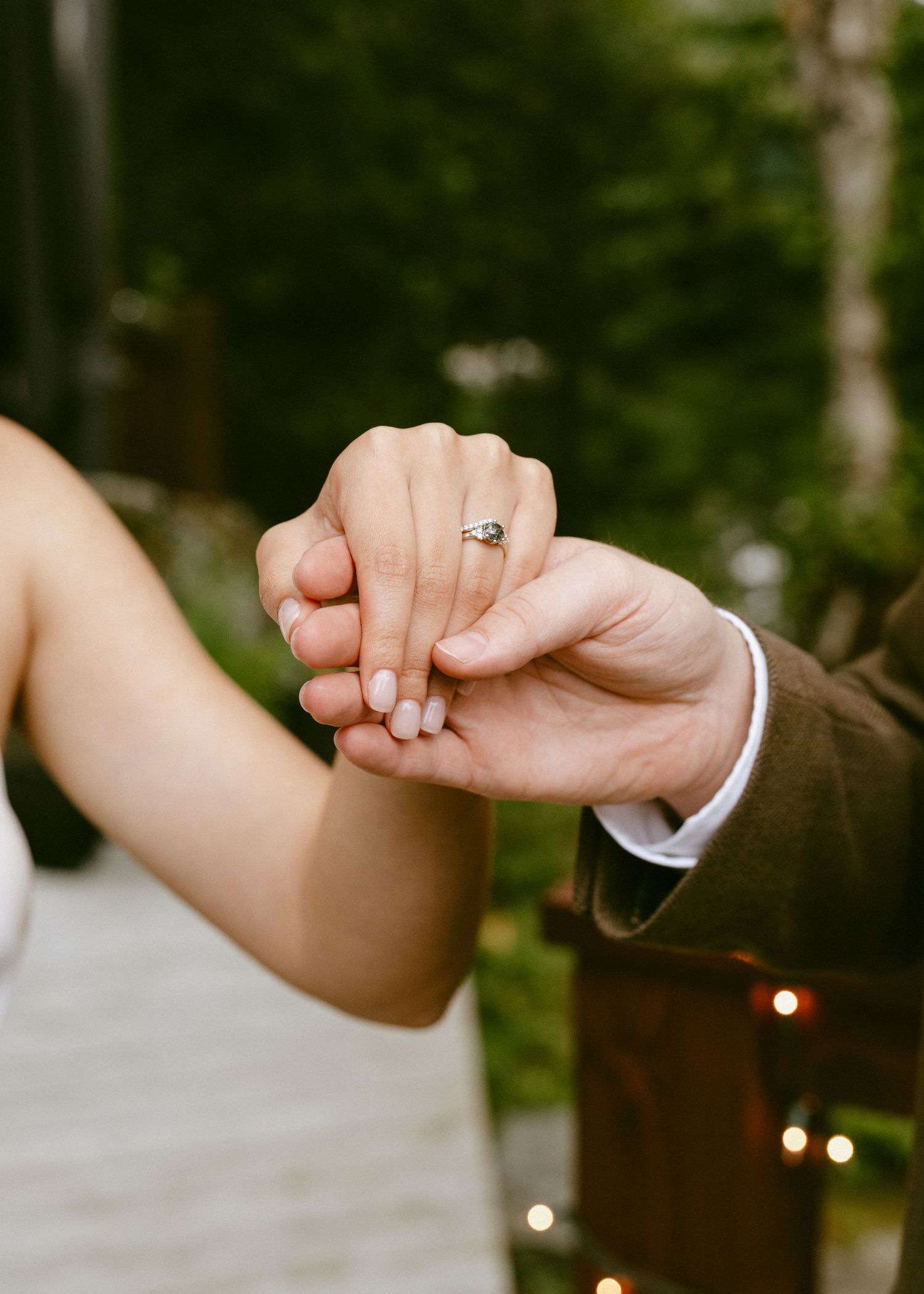 Close-up of bride and groom holding hands showing engagement ring at outdoor wedding ceremony.