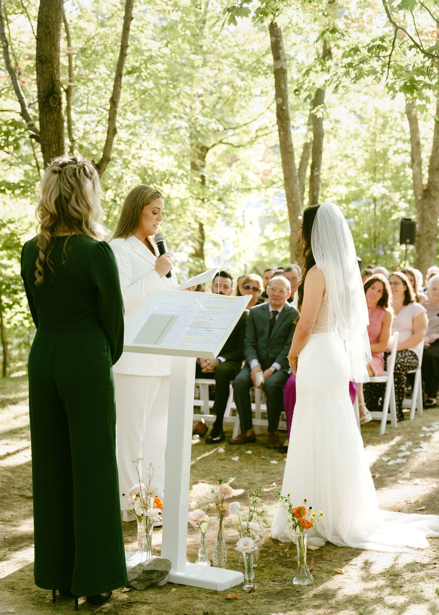 Bride in white dress standing at altar during outdoor woodland wedding ceremony.