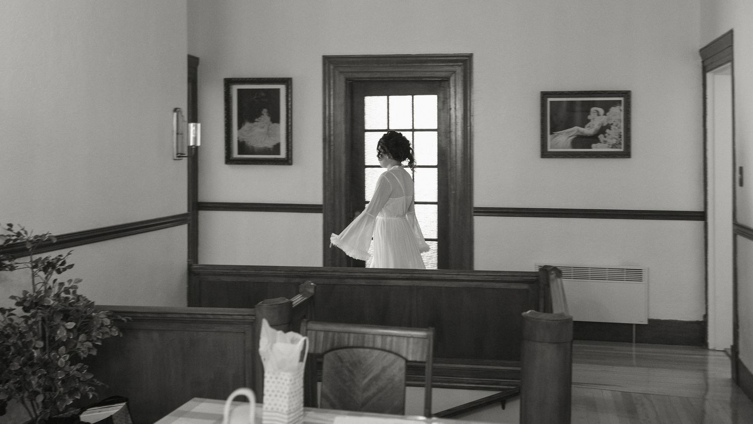 Black and white photo of a woman in white dress walking through a doorway in a classic interior room.