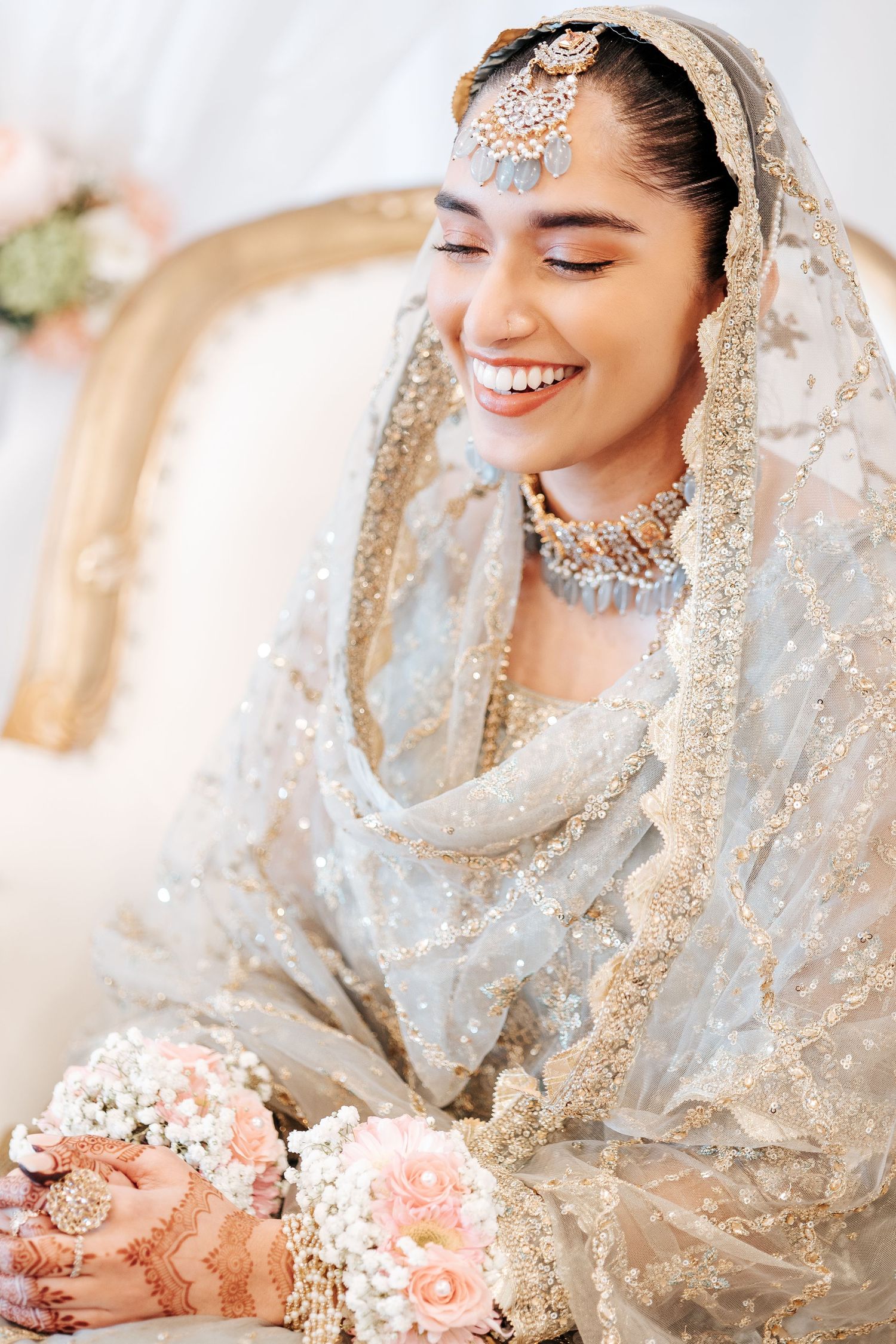 Radiant South Asian bride smiling in silver embroidered dupatta with pearl and gold bridal jewelry.