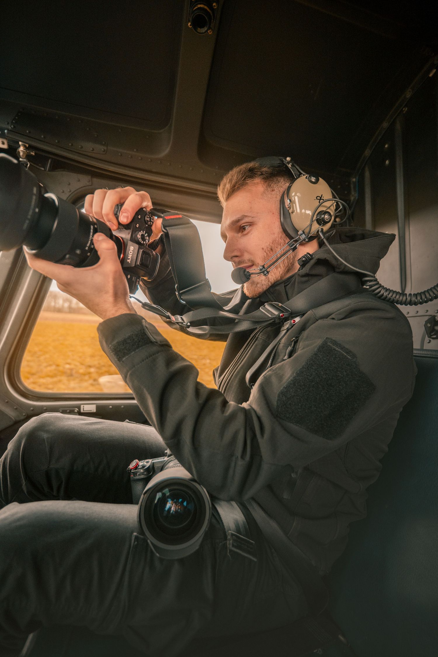 Aerial photographer in flight helmet reviews camera shots inside helicopter cockpit.