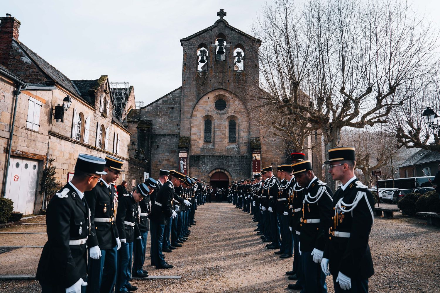 French gendarmerie officers in dress uniform form a ceremonial honor guard outside a historic stone church.