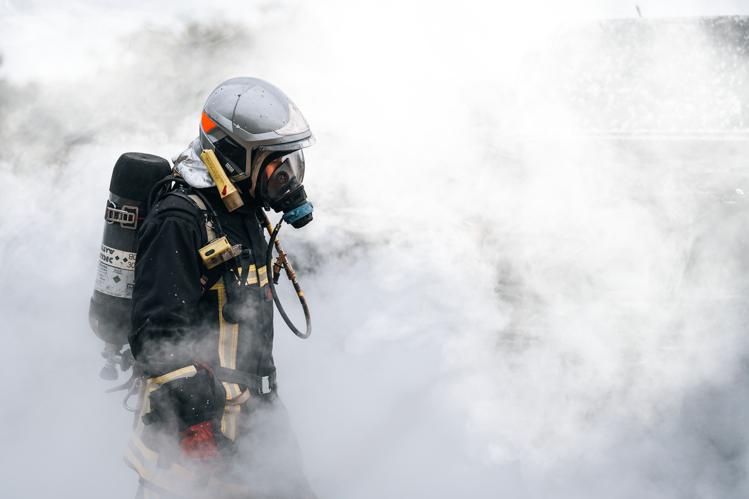 Firefighter in full protective gear and oxygen tank navigating through dense white smoke during an emergency rescue operation.