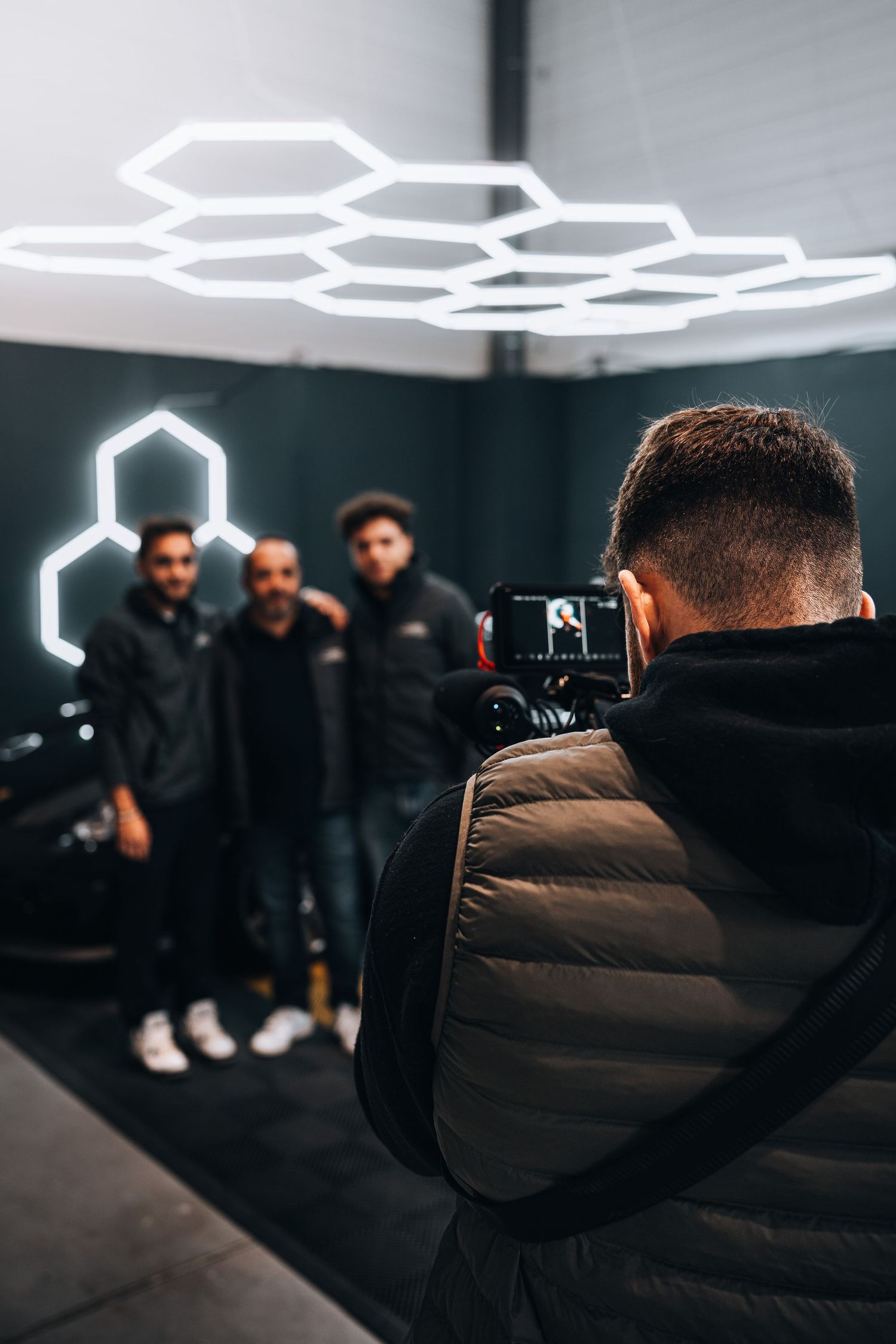 Photographer captures three men posing in a dark studio with geometric hexagonal neon lighting.