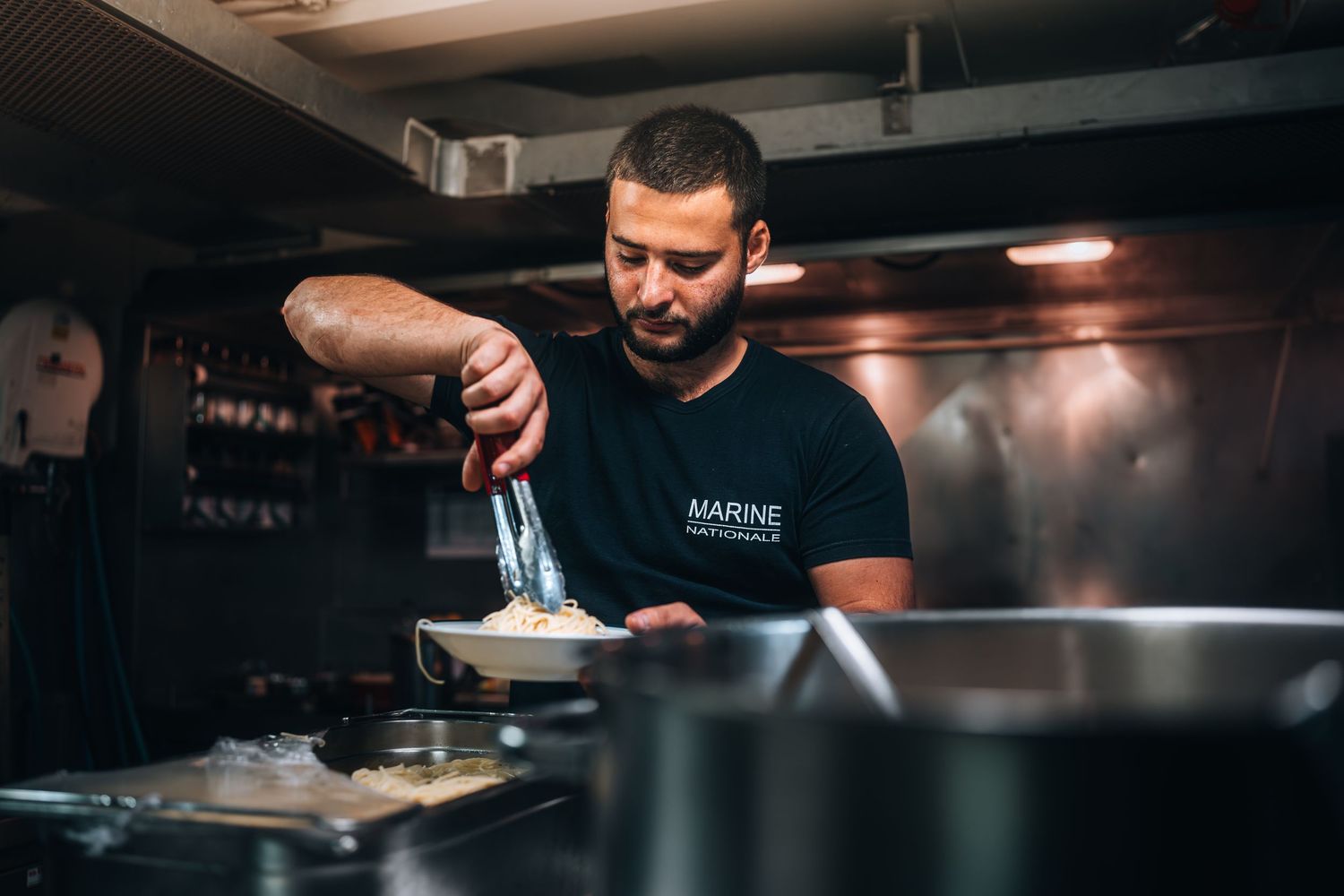 Male chef plating food in dimly lit professional kitchen with steam rising.
