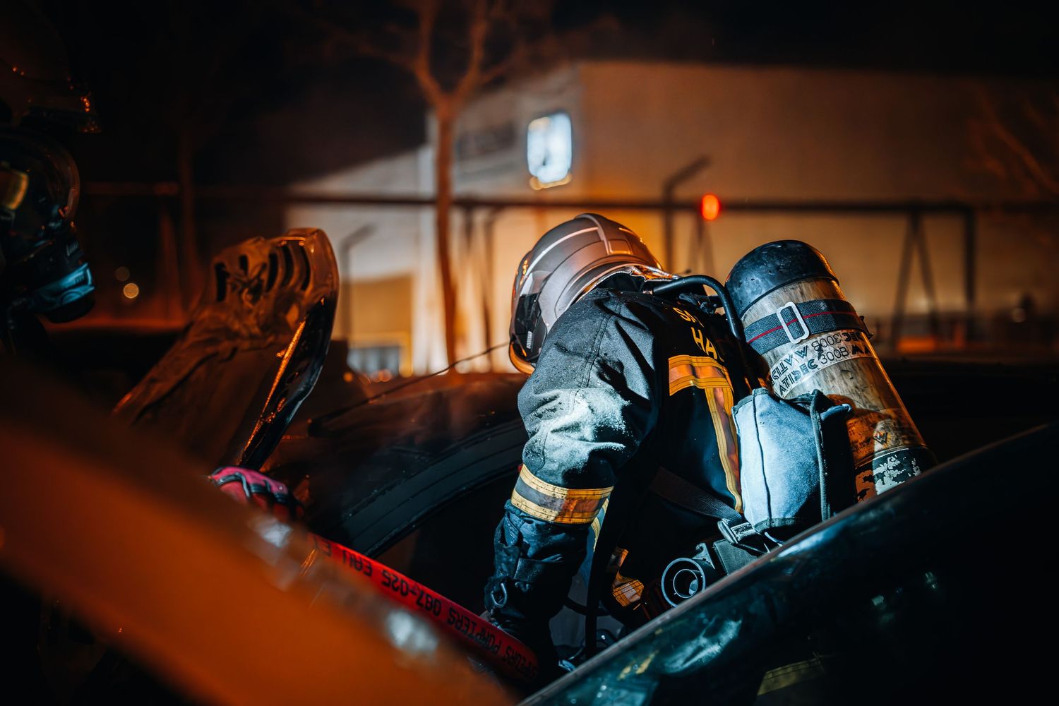 Two firefighters in breathing apparatus working together during nighttime rescue operation.