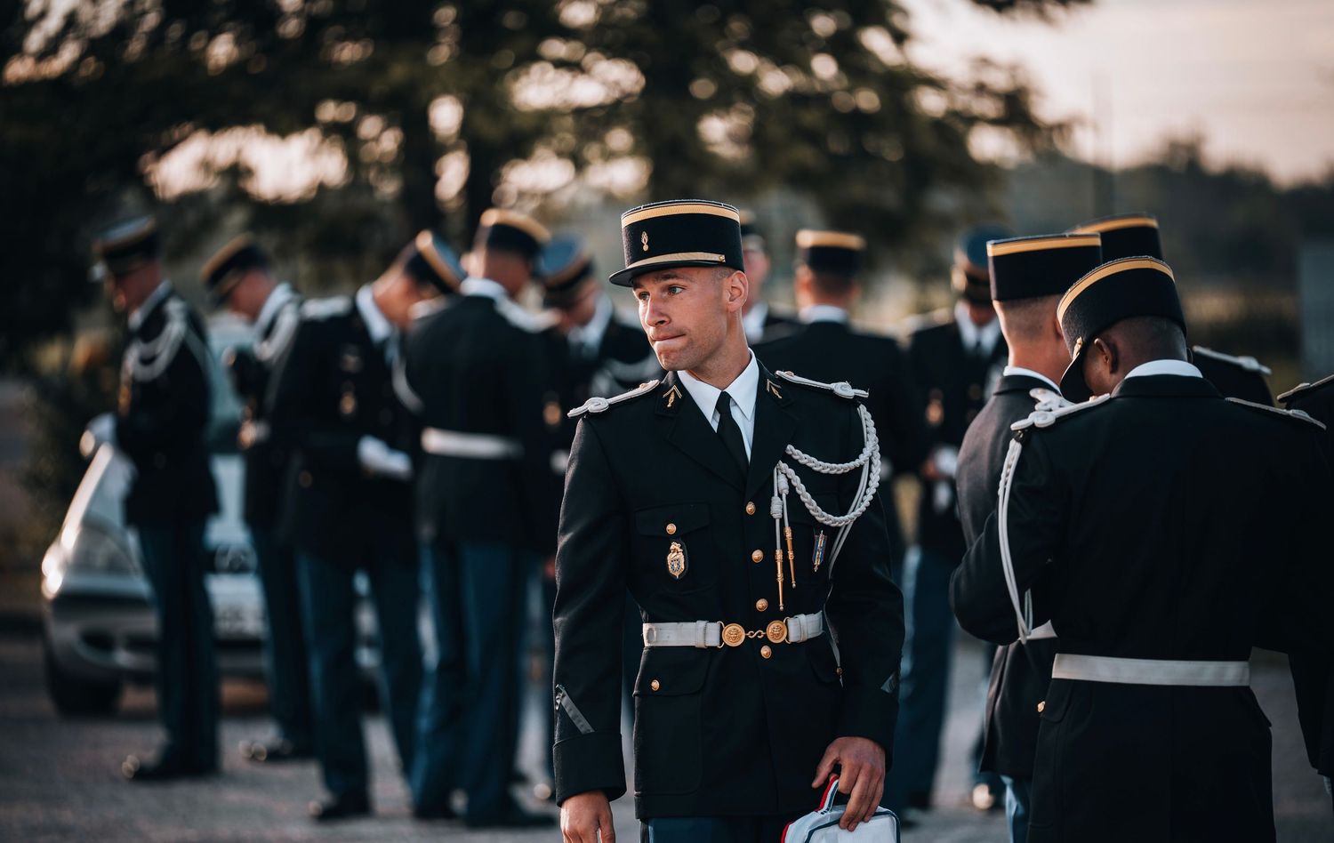 Military officers in dark uniforms stand at attention during an outdoor ceremony at dusk.