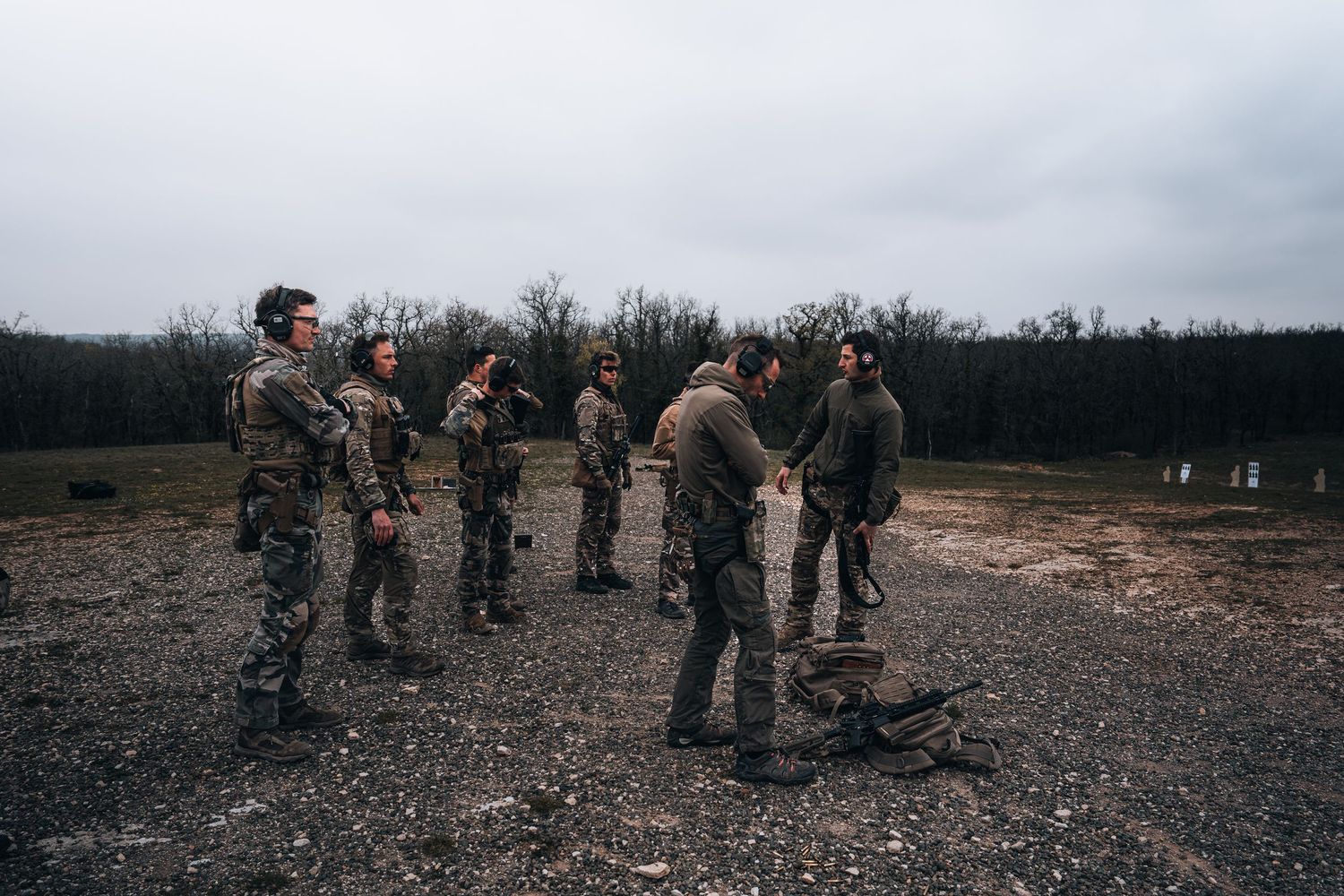 Group of soldiers in tactical gear gathered at outdoor military training range.