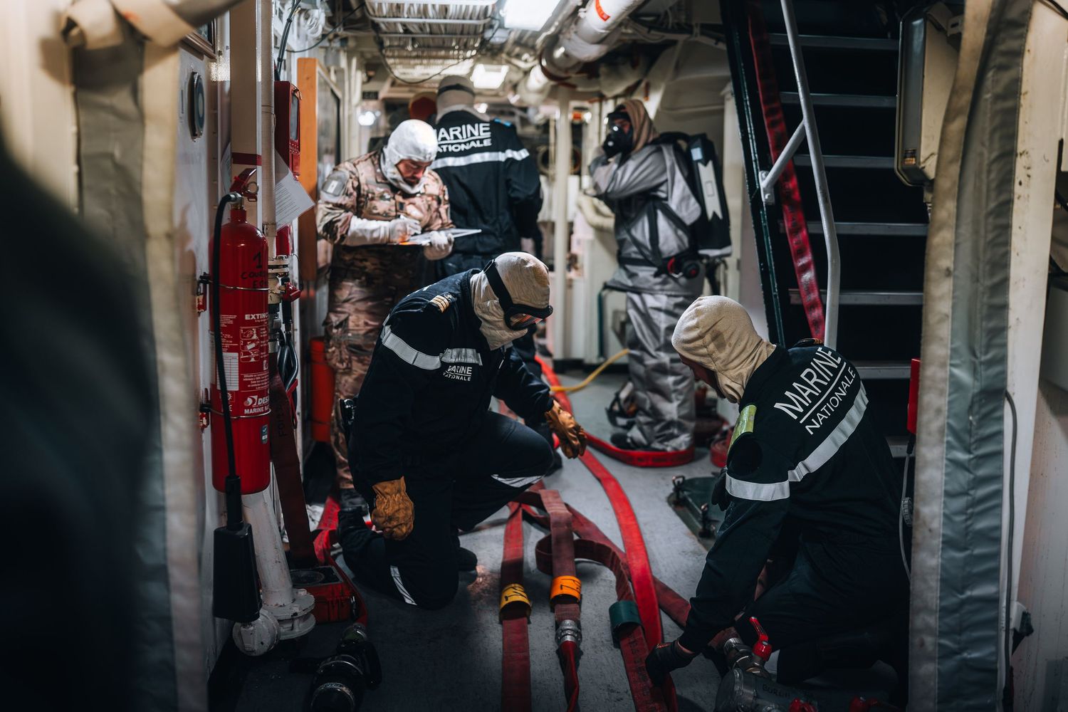 Marine rescue team in uniform carrying stretcher through narrow ship corridor.