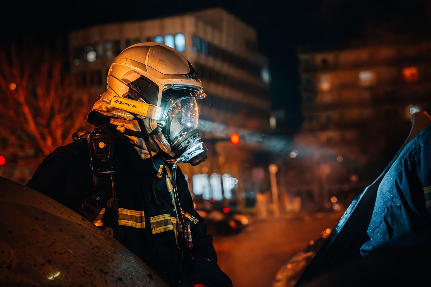French firefighter in helmet and face shield on duty during nighttime urban emergency.