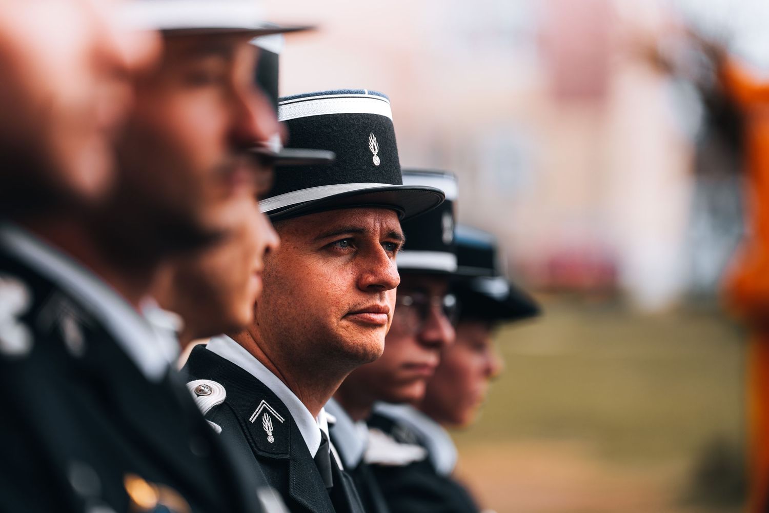 Row of military officers in formal black uniforms with decorative hats standing at attention outdoors.