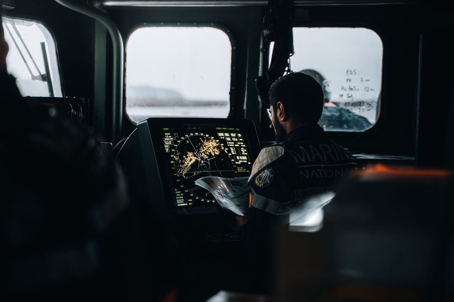 Military crew member working at navigation console aboard warship bridge during sea operation.
