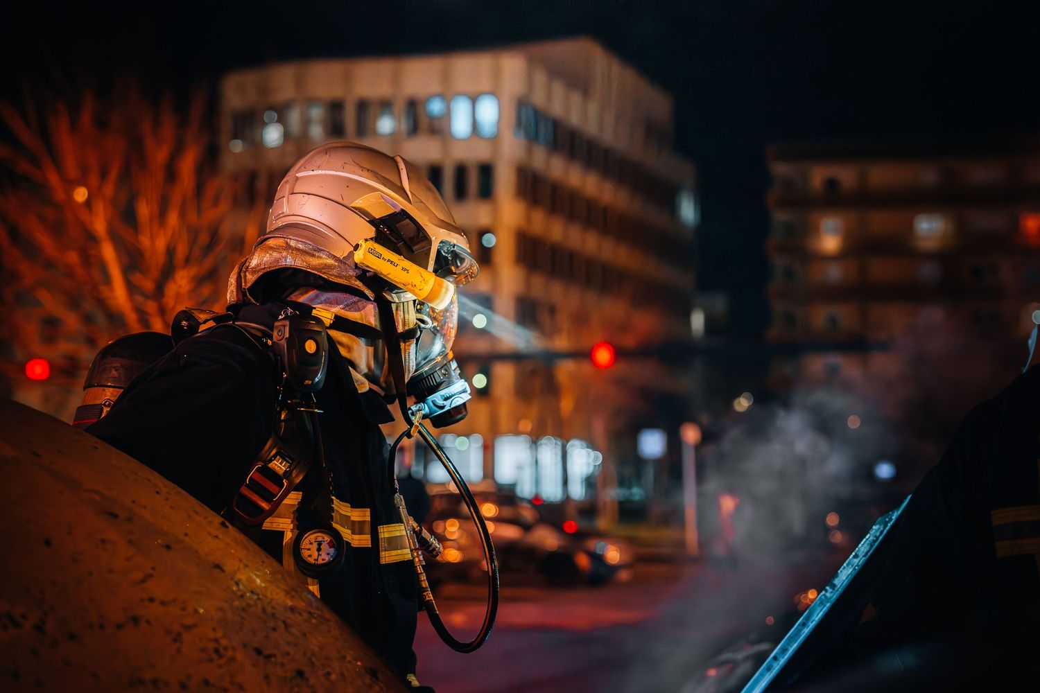 A lone firefighter in full protective gear and breathing apparatus crouches on a rooftop at night amid smoke.