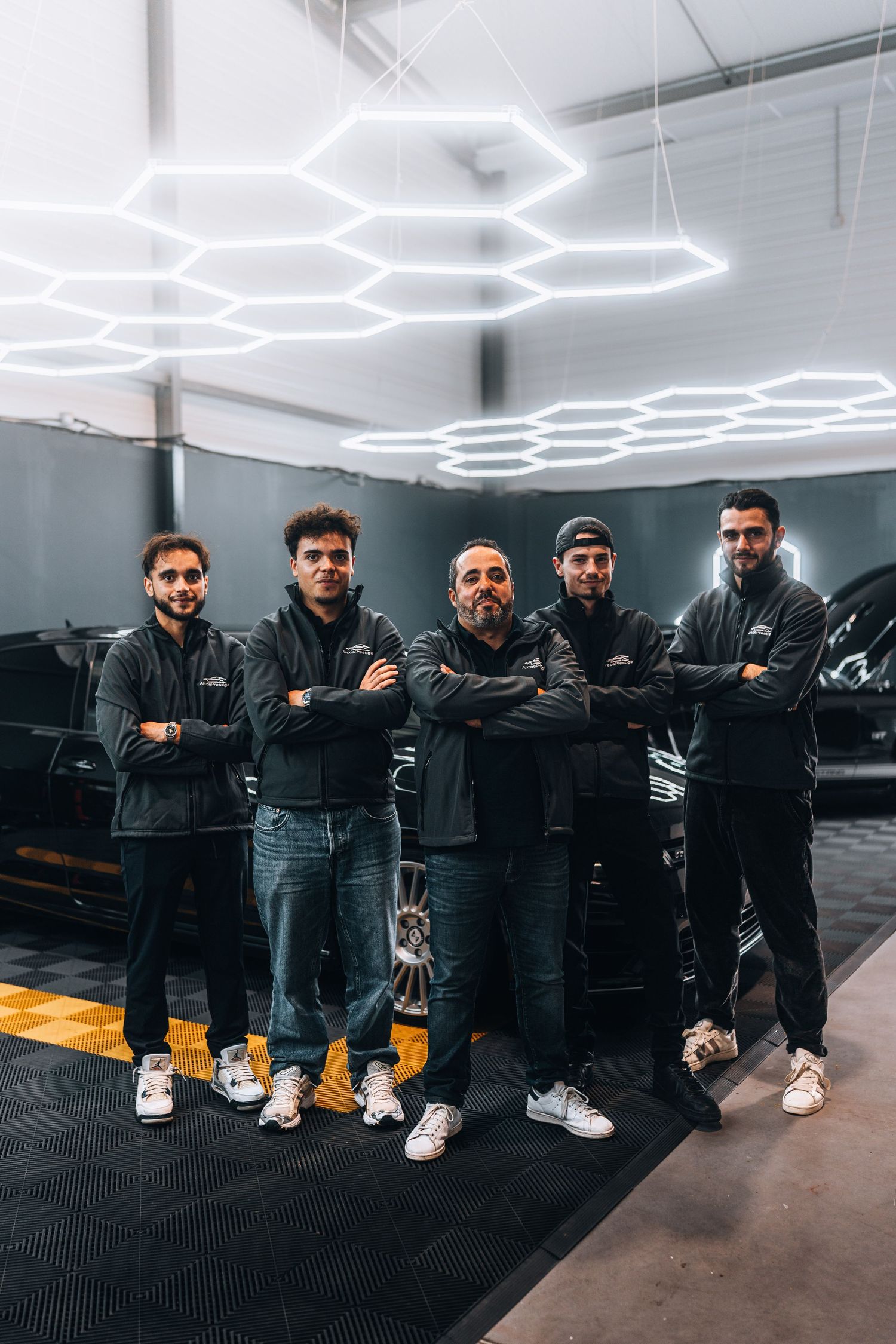 Five auto detailing professionals pose with arms crossed in a modern garage with hexagonal LED lights.