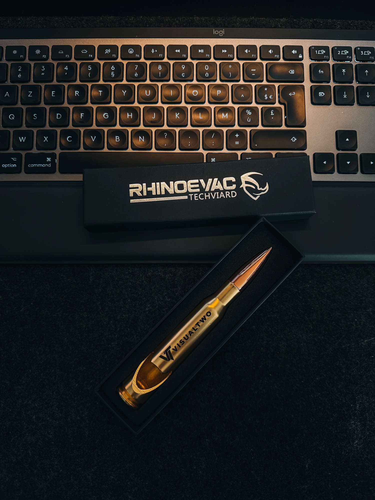 RhinoVac Techviard gold bullet-shaped USB drive in black box beside a backlit gaming keyboard.