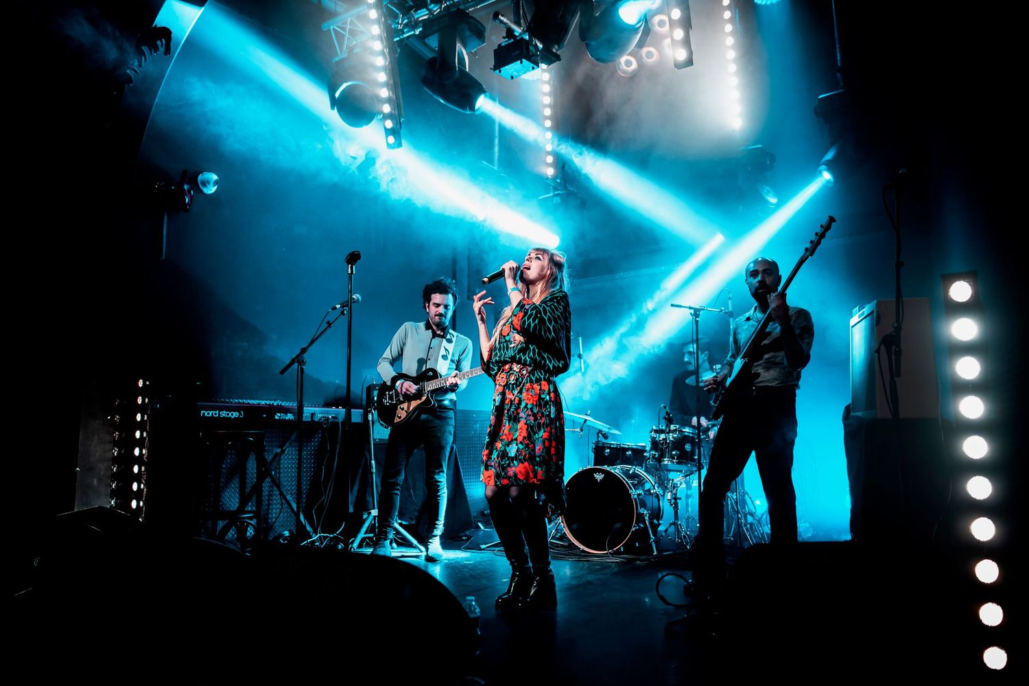 Female vocalist performs on stage with band under dramatic blue spotlights at a live concert.