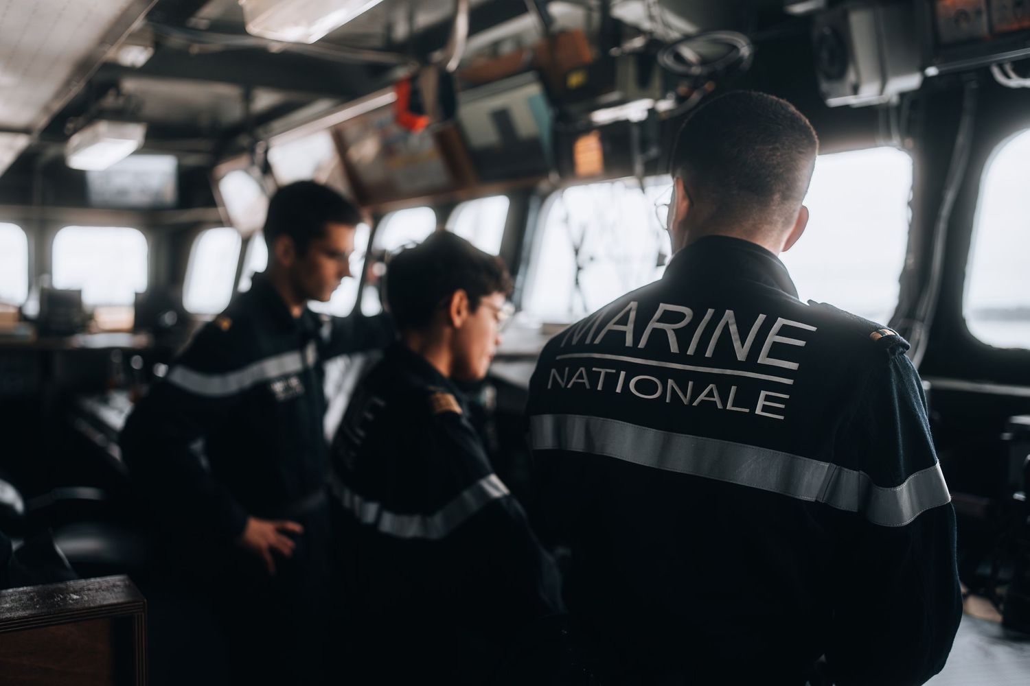 French Marine Nationale sailors in uniform stand on the bridge of a naval vessel at sea.