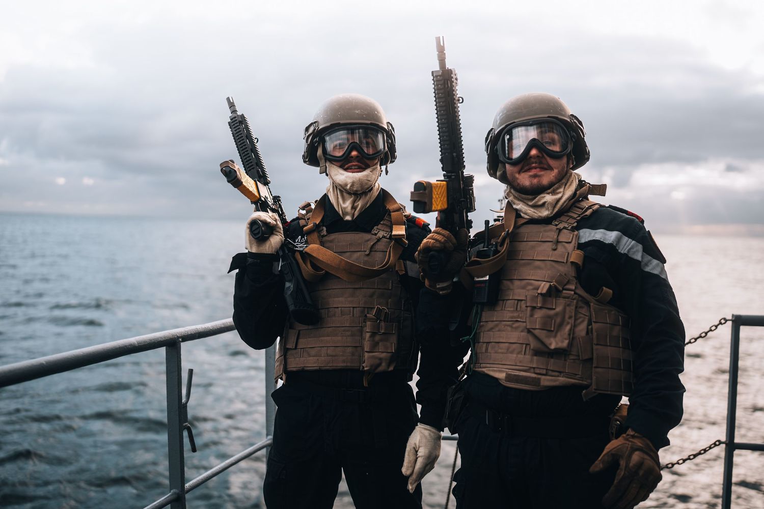 Two armed naval soldiers in tactical gear and helmets pose on a military ship deck.