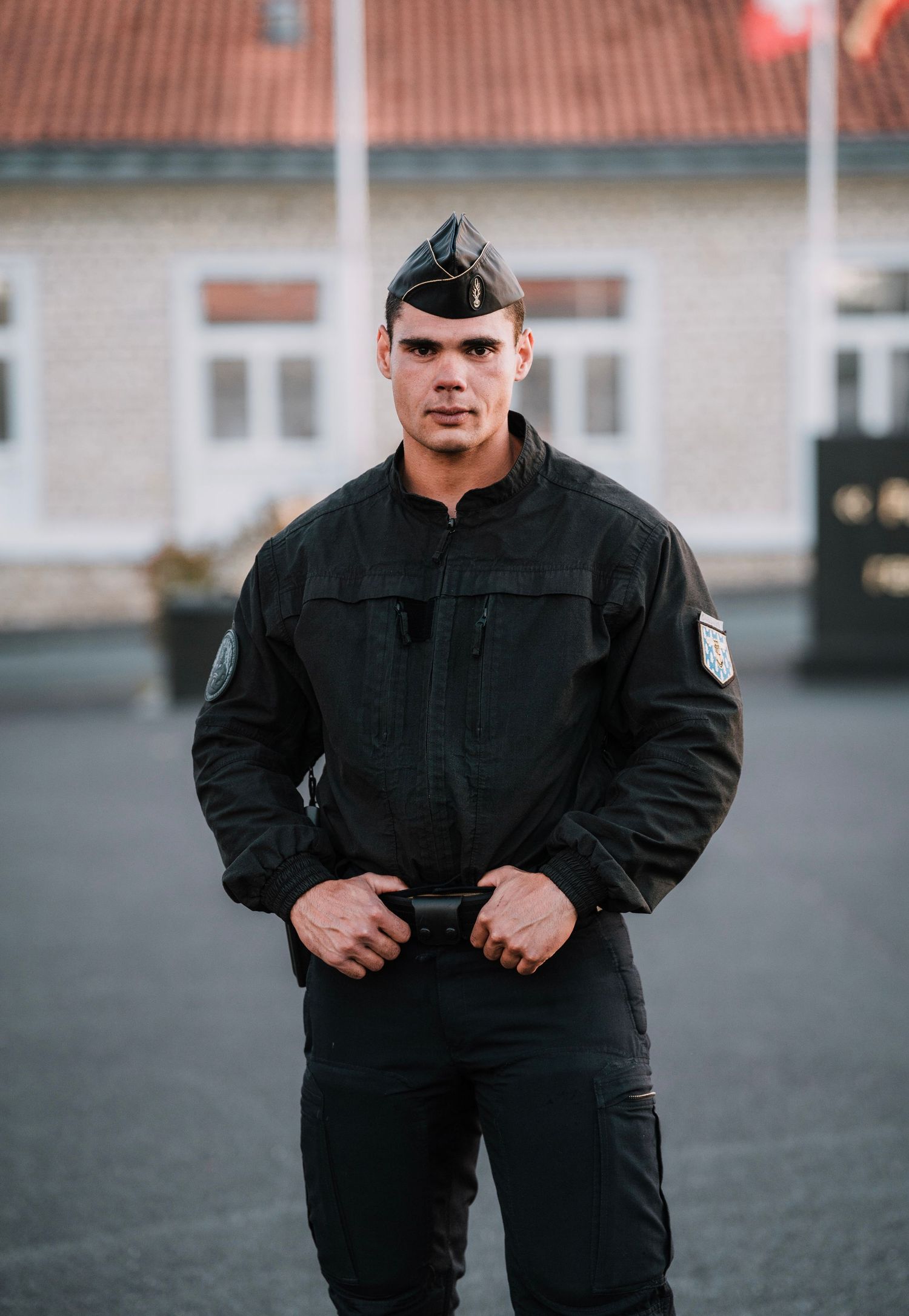 Young male officer in black uniform and garrison cap stands confidently in a courtyard.