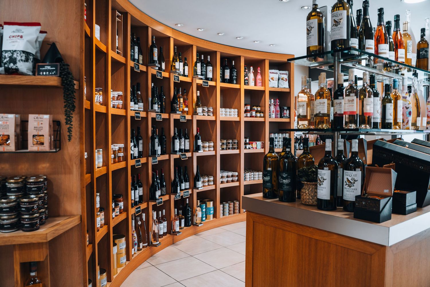 Curved wooden shelves stocked with wine bottles and specialty foods in a boutique liquor store.