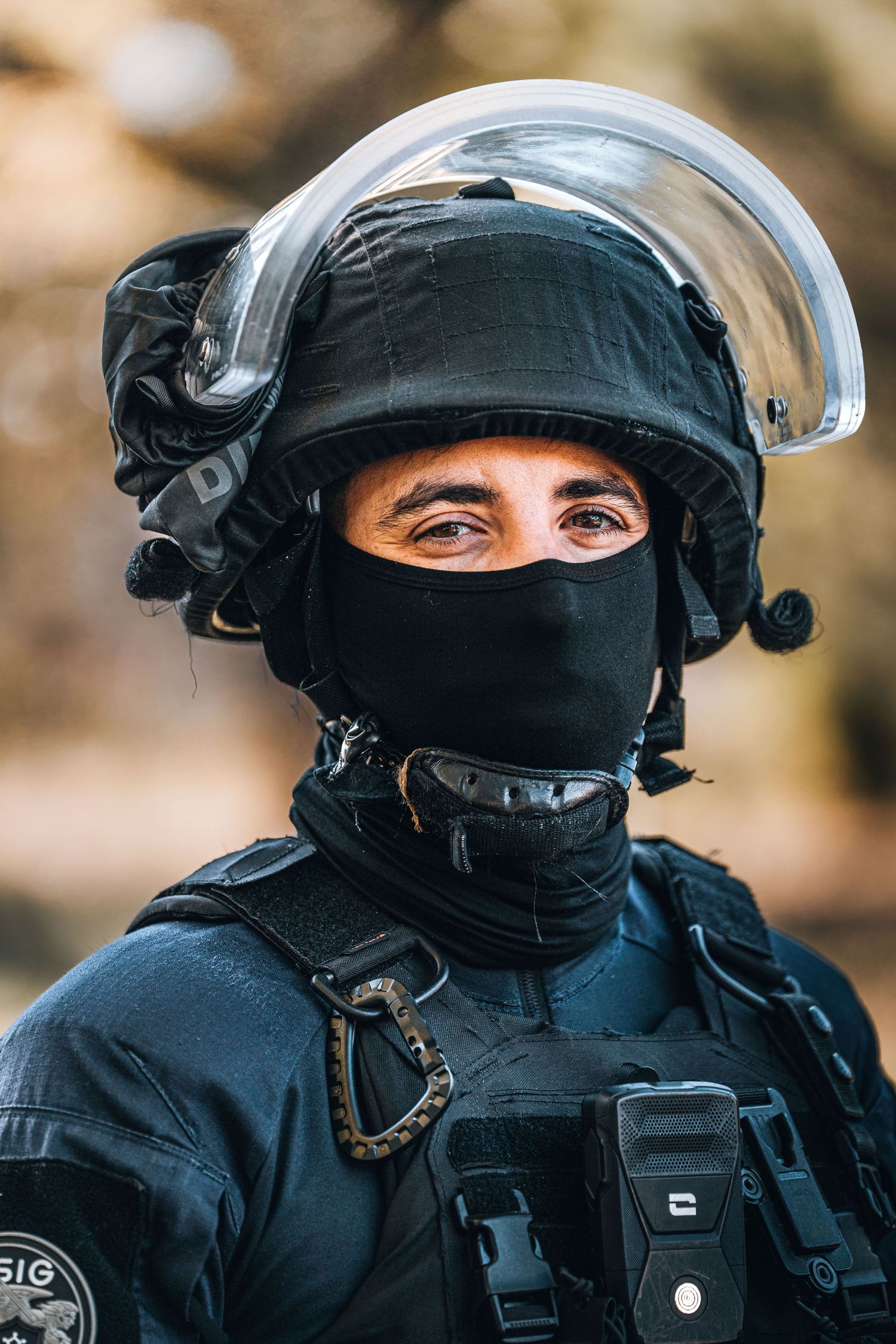 SWAT officer in full black tactical gear with riot helmet and face mask looking at camera.