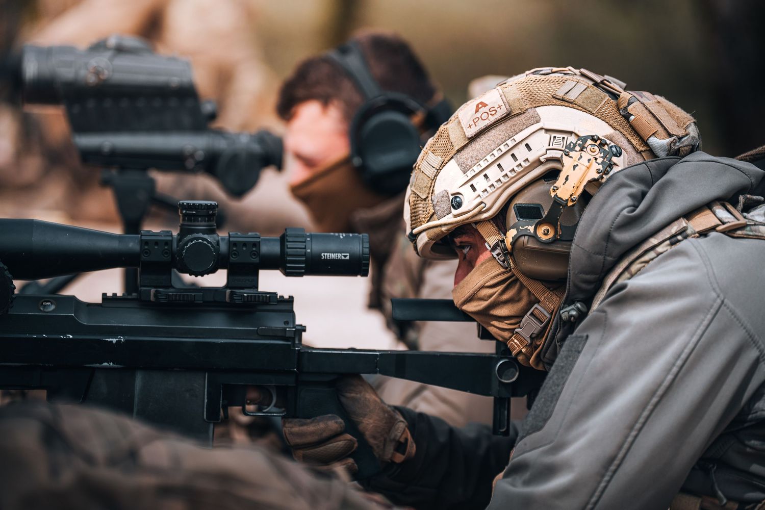 Military sniper in tactical helmet aiming rifle with scope during field operation.
