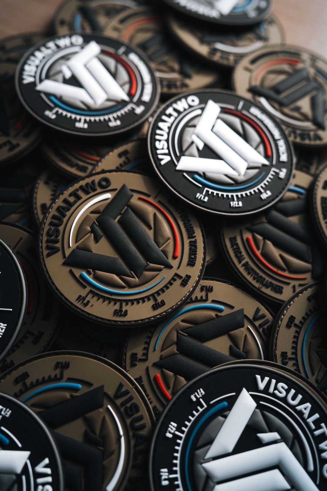 Pile of VISUALTWO branded PVC patch coins with black and tan design on wooden surface.