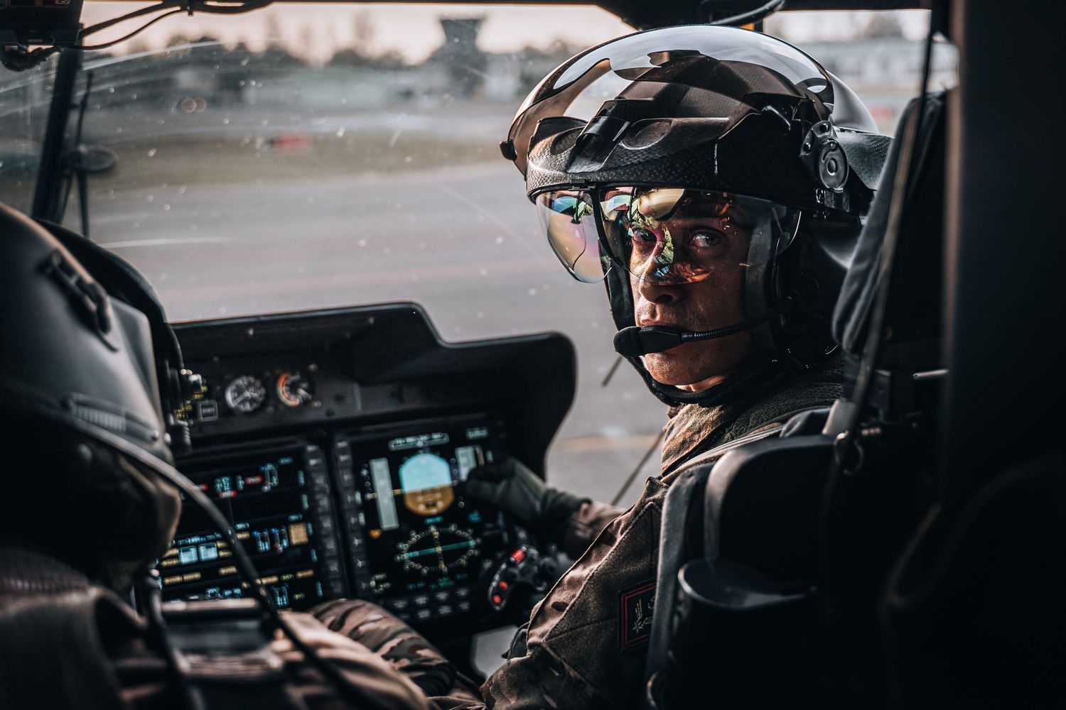 Military helicopter pilot in cockpit with helmet and glasses ready for flight.