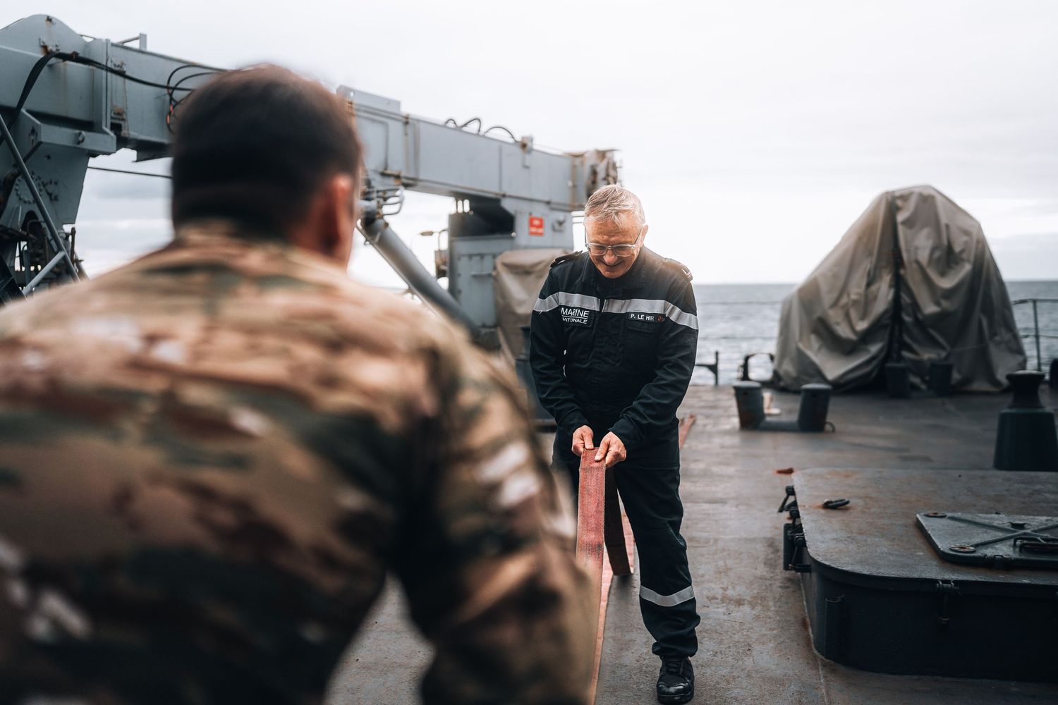 Two crew members handling rope on ship deck with ocean visible in background.